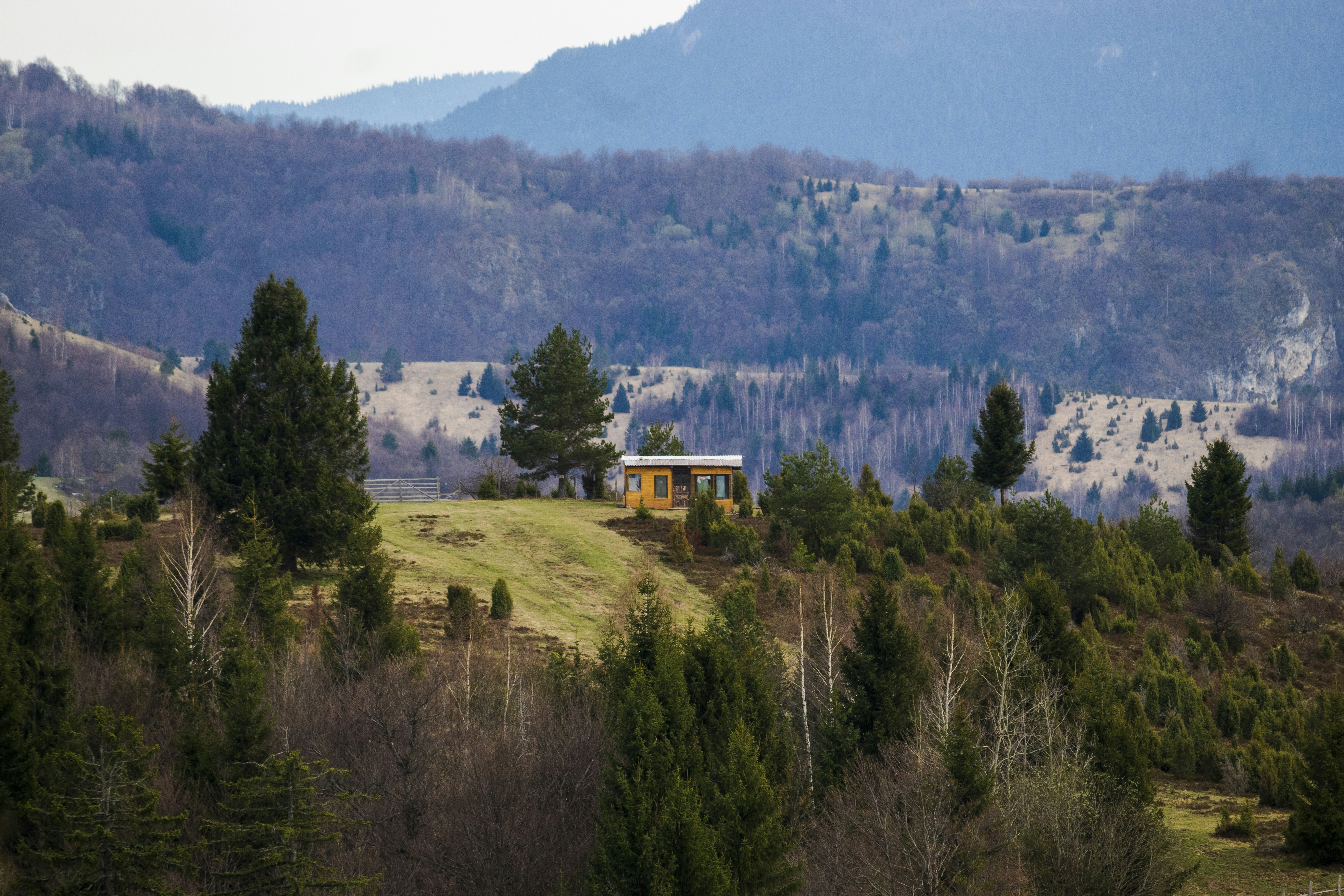 The exterior of a stunning modern home with large windows, set against a beautiful backdrop of rolling green hills, representing a desirable property in a scenic area.