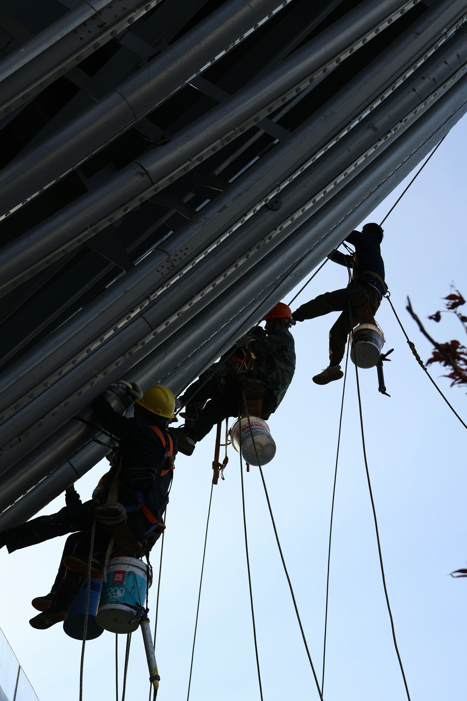 Workers suspended by ropes painting a tall structure
