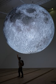 A person stands beneath a large, illuminated moon installation.
