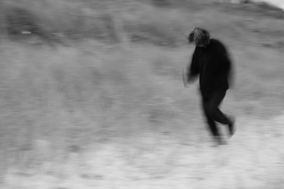 Person runs through tall grass on dirt road, wearing black jacket and pants