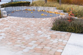 Paved walkway with stone seating area and autumn leaves.