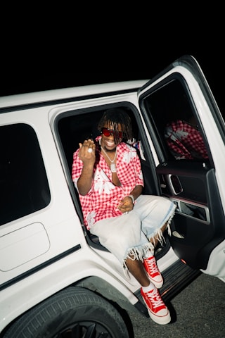 Man in red shirt and denim shorts in white car