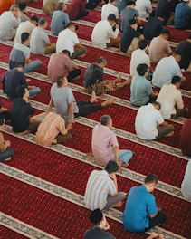 Men praying together on a red carpeted floor.