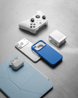 White gaming controller, smartphone, and earbuds on surface.