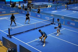 Four people play pickleball on a blue court.