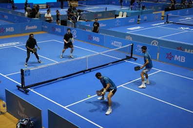 Four people play pickleball on a blue court.