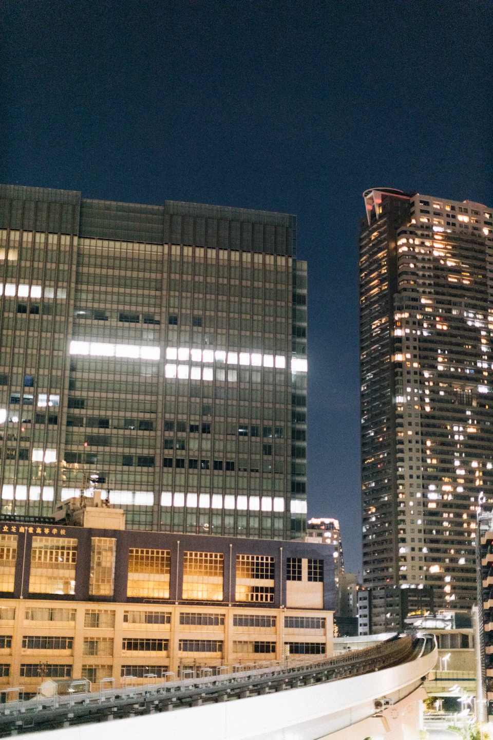 Two towering buildings stand side by side on either side of a bridge at night