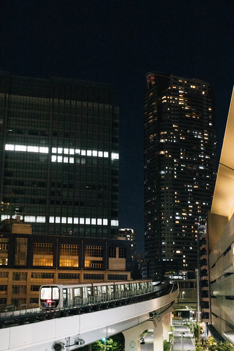 Train crosses elevated track through city center at night with bright cityscape illumination