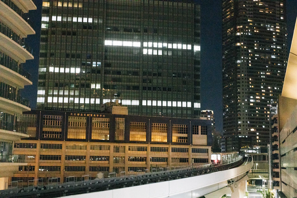 Cityscape at night with tall buildings illuminated by bright lights against dark sky