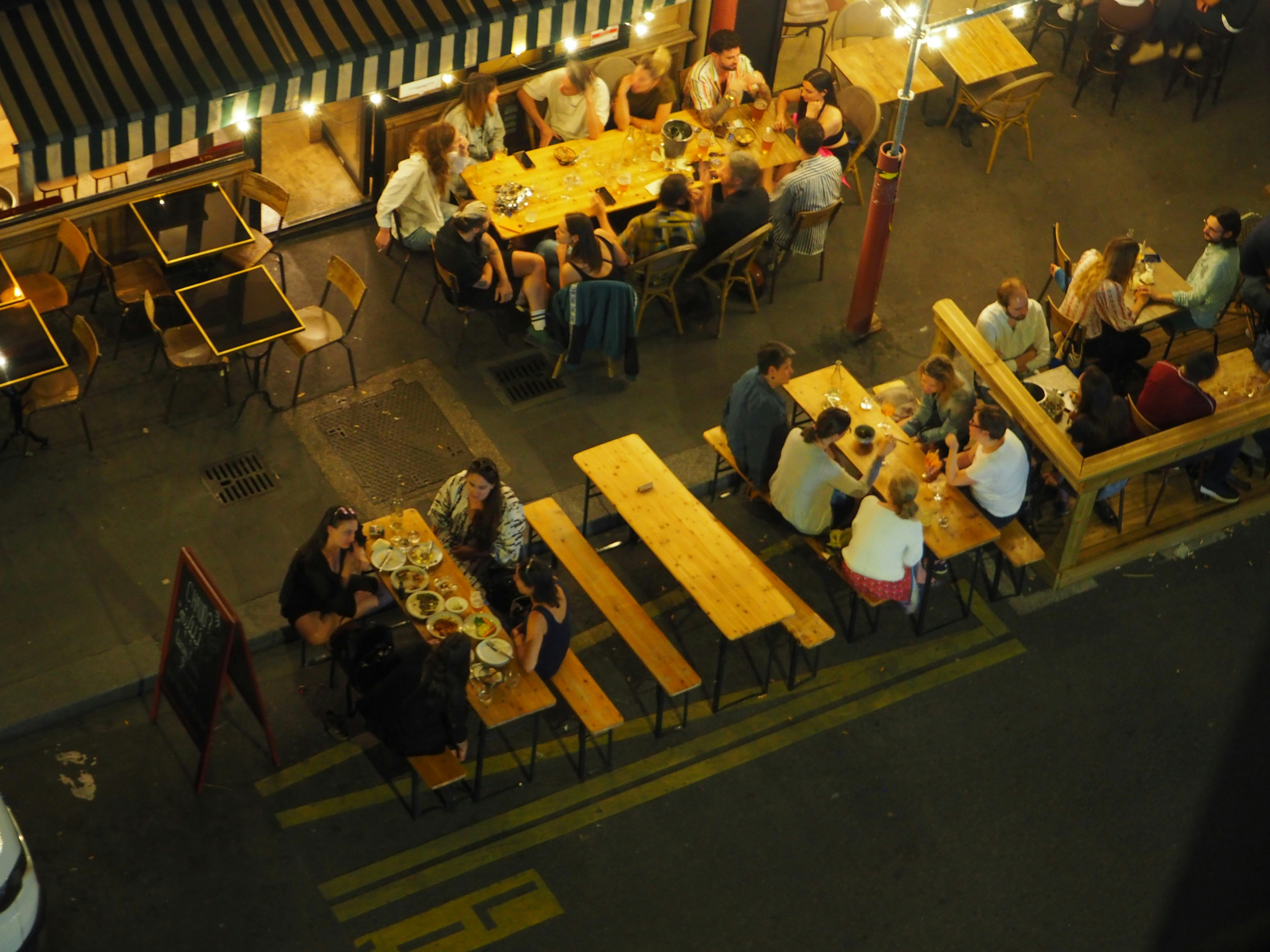 An aerial view of people dining at outdoor tables on a city street