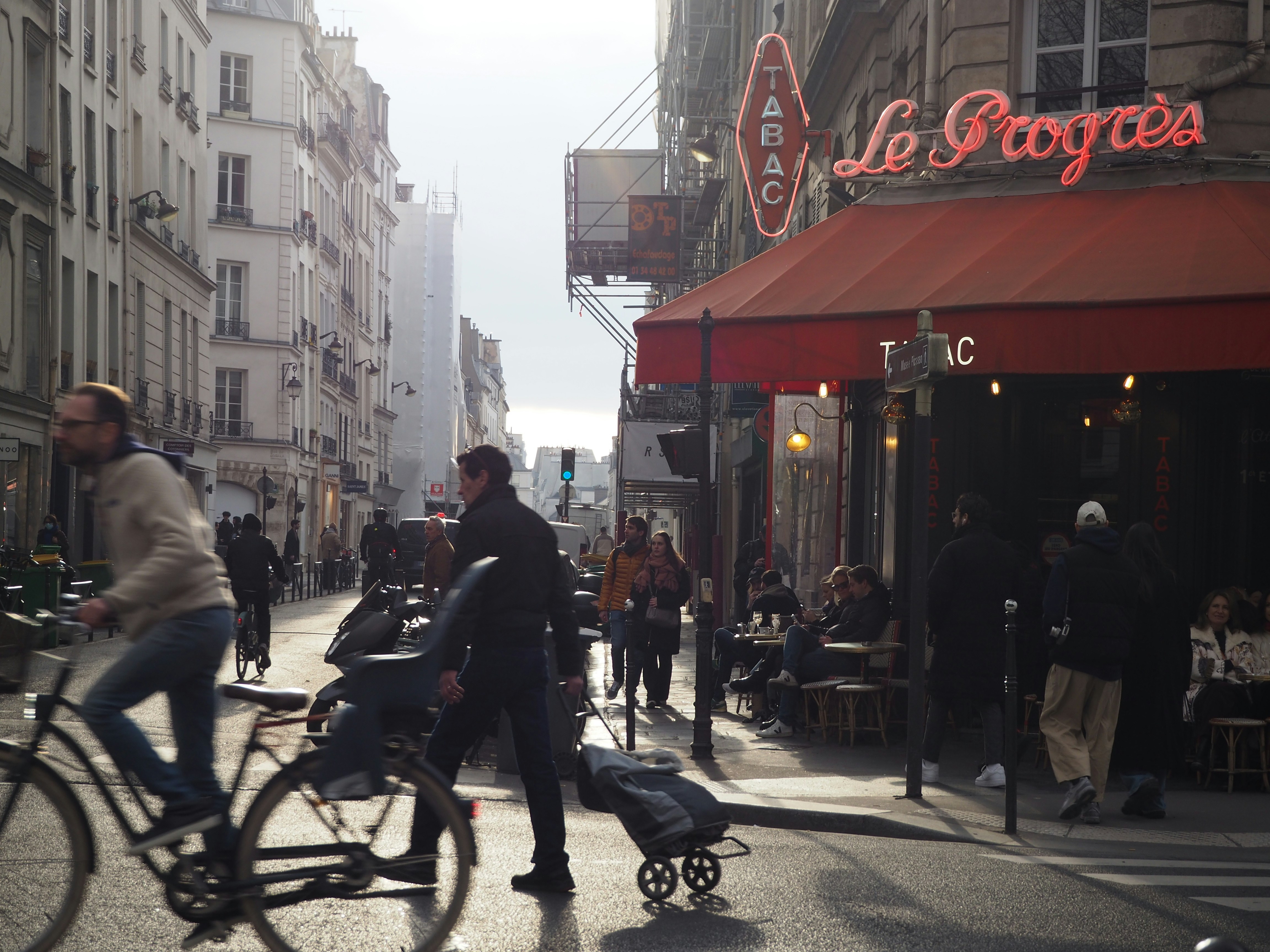 A person cycling past a cafe with a red awning in Paris
