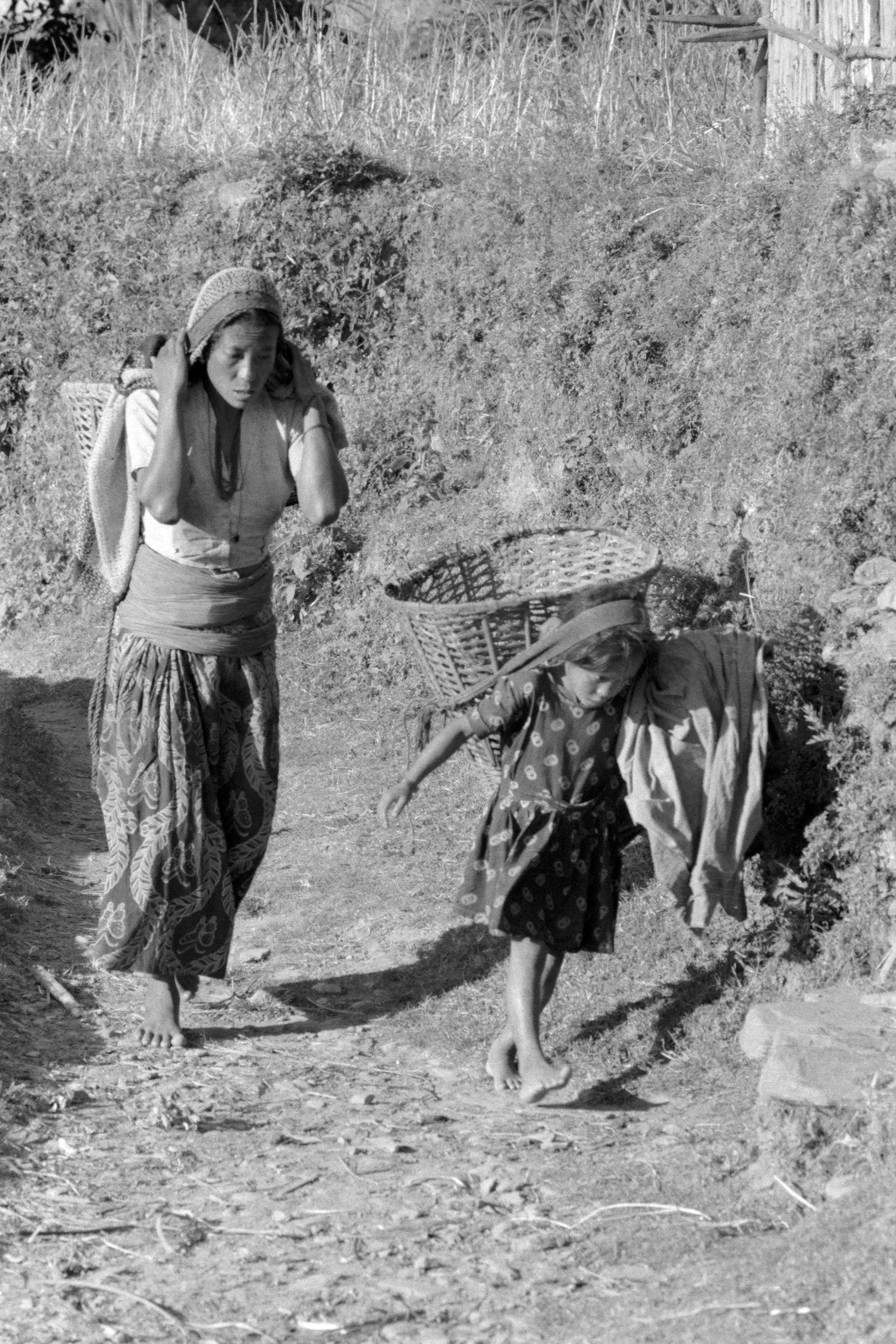 Woman and child carrying baskets on a dirt path