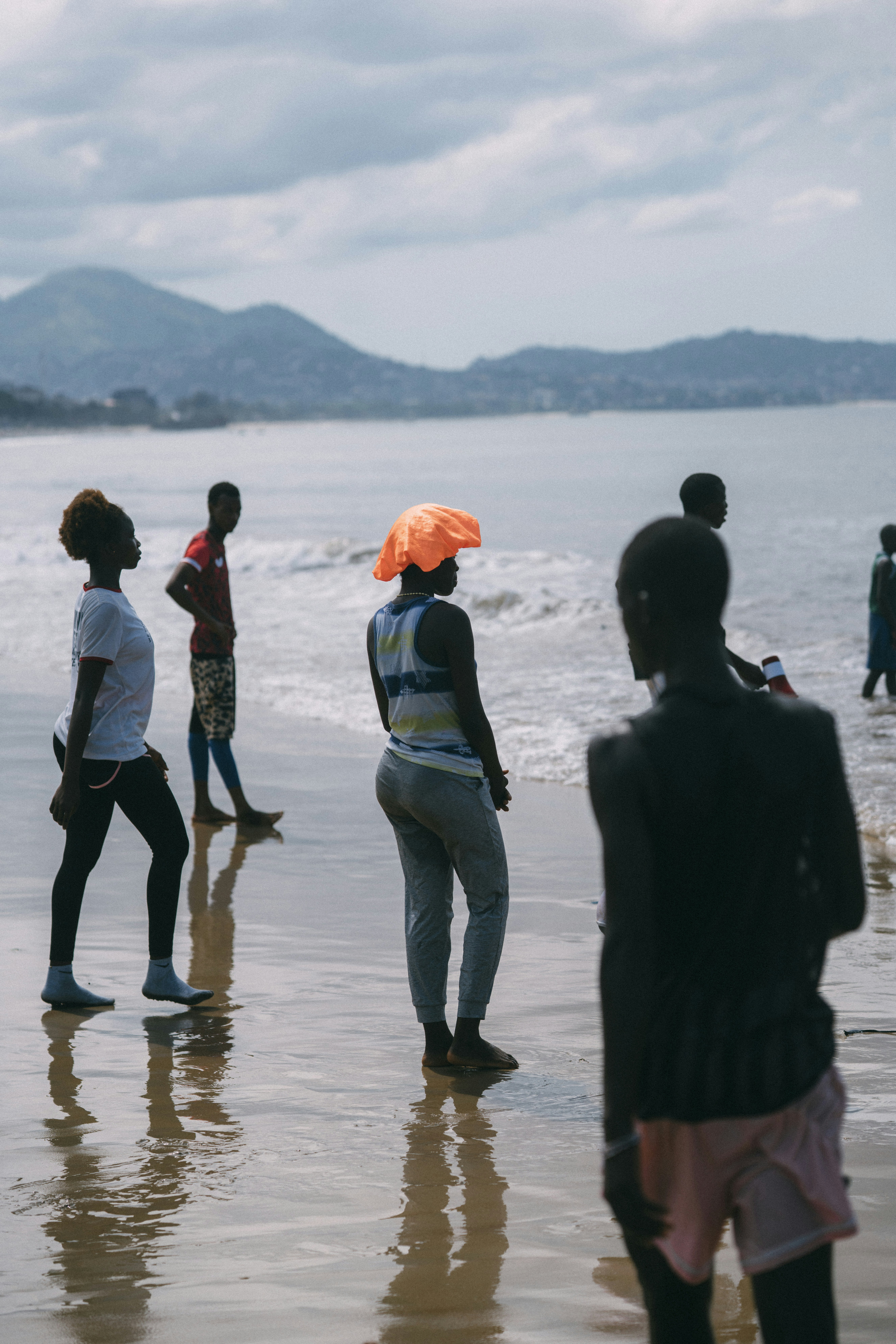 People standing on a wet beach with mountains behind.