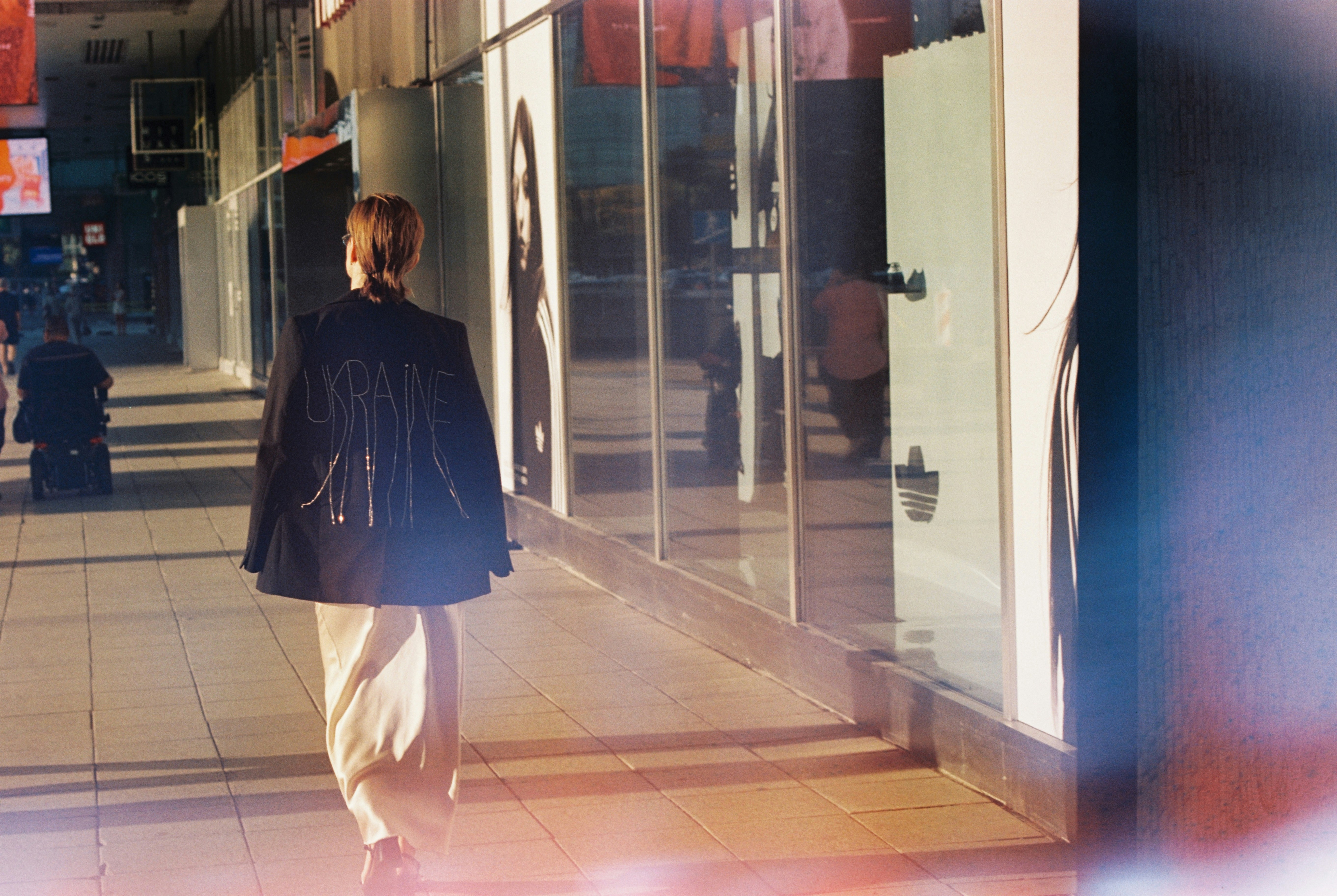 Woman walking down a sunlit sidewalk past storefronts