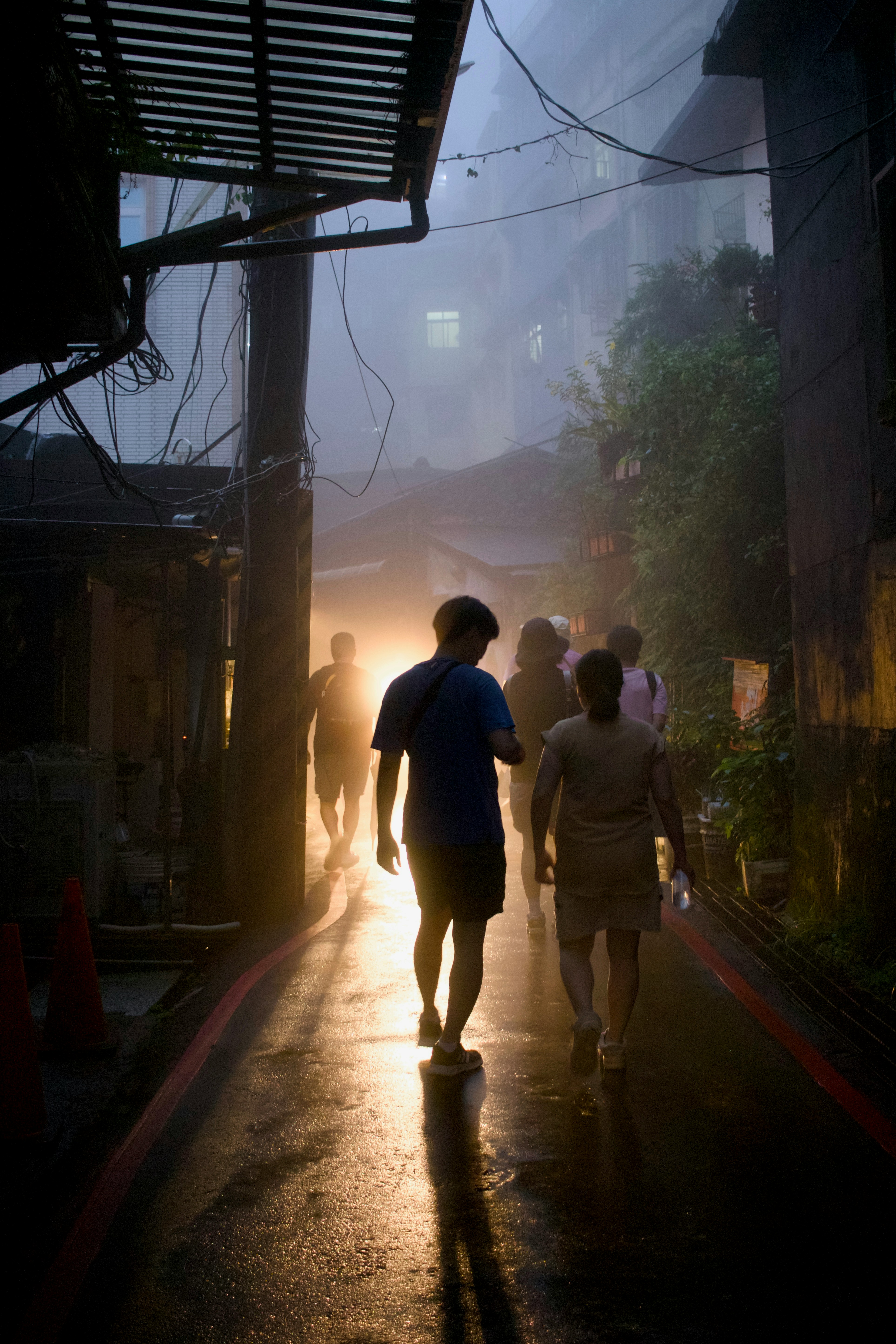 People walk down a misty, dimly lit alleyway.
