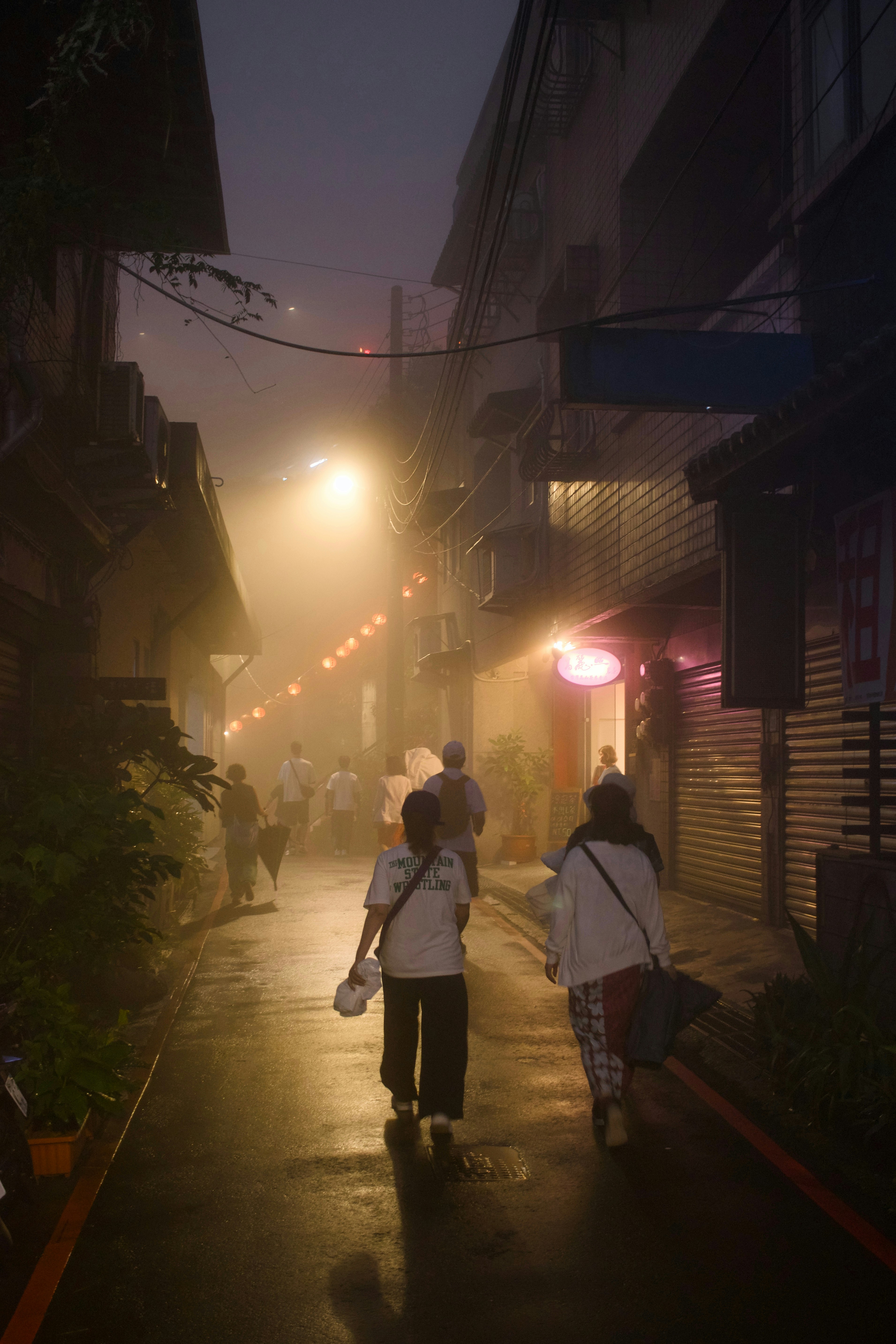 People walk down a foggy street at night.