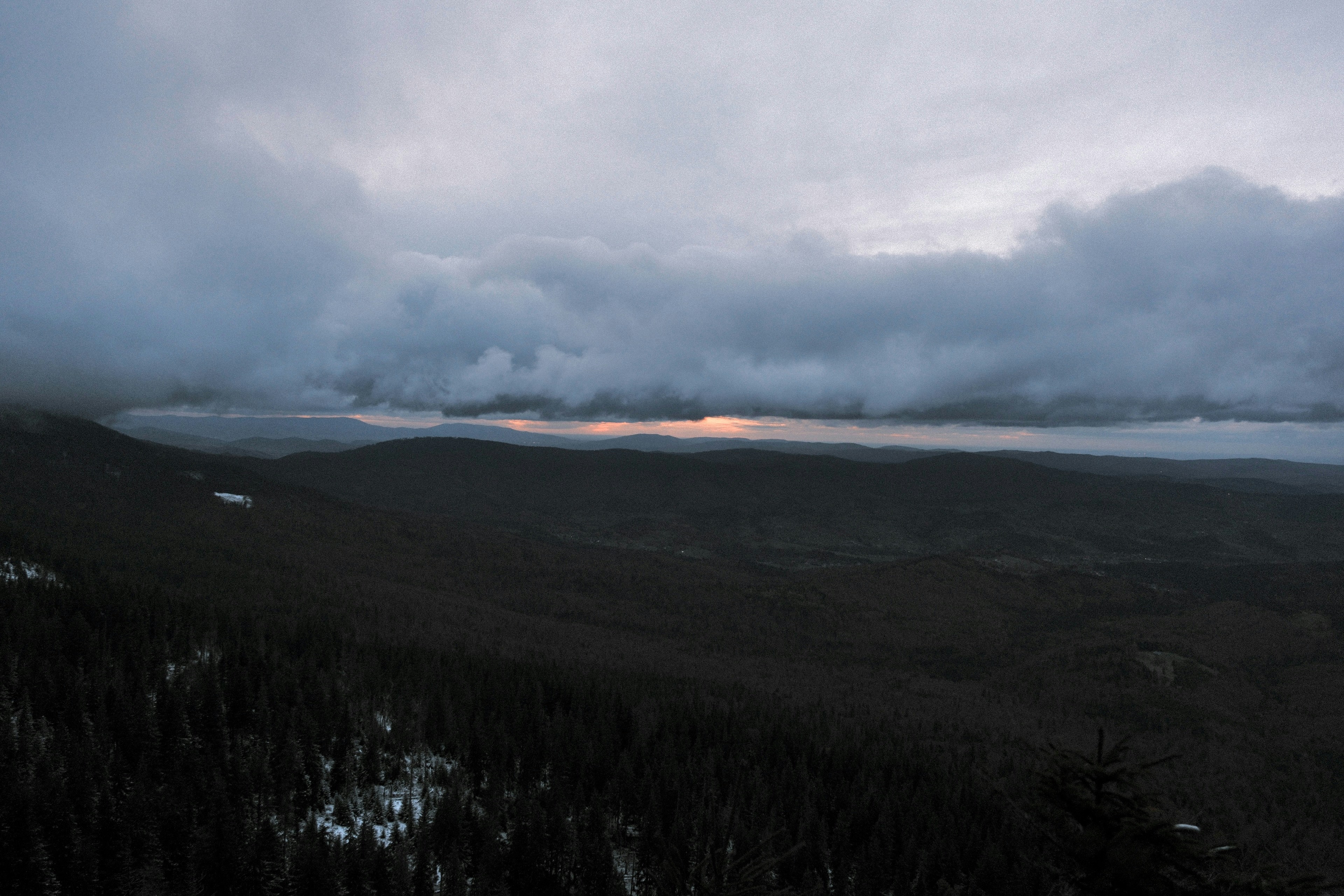 Dark clouds over a vast, forested mountain landscape.