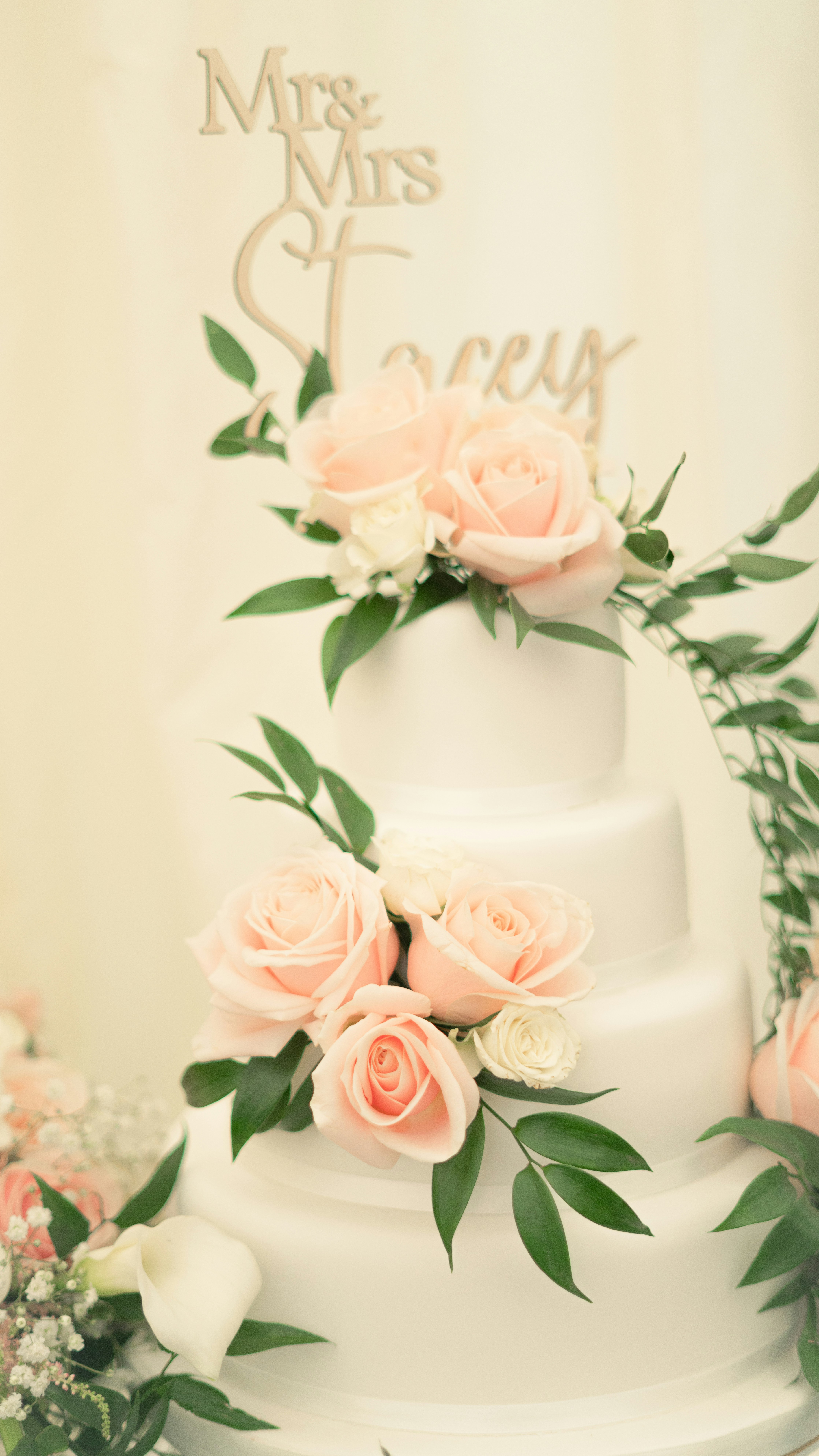 A white wedding cake with pink roses and greenery.