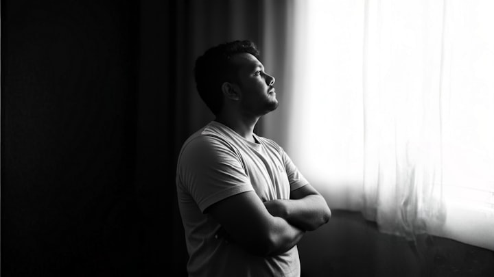 A person at a window with arms crossed, considered posture, side light, anonymized framing
