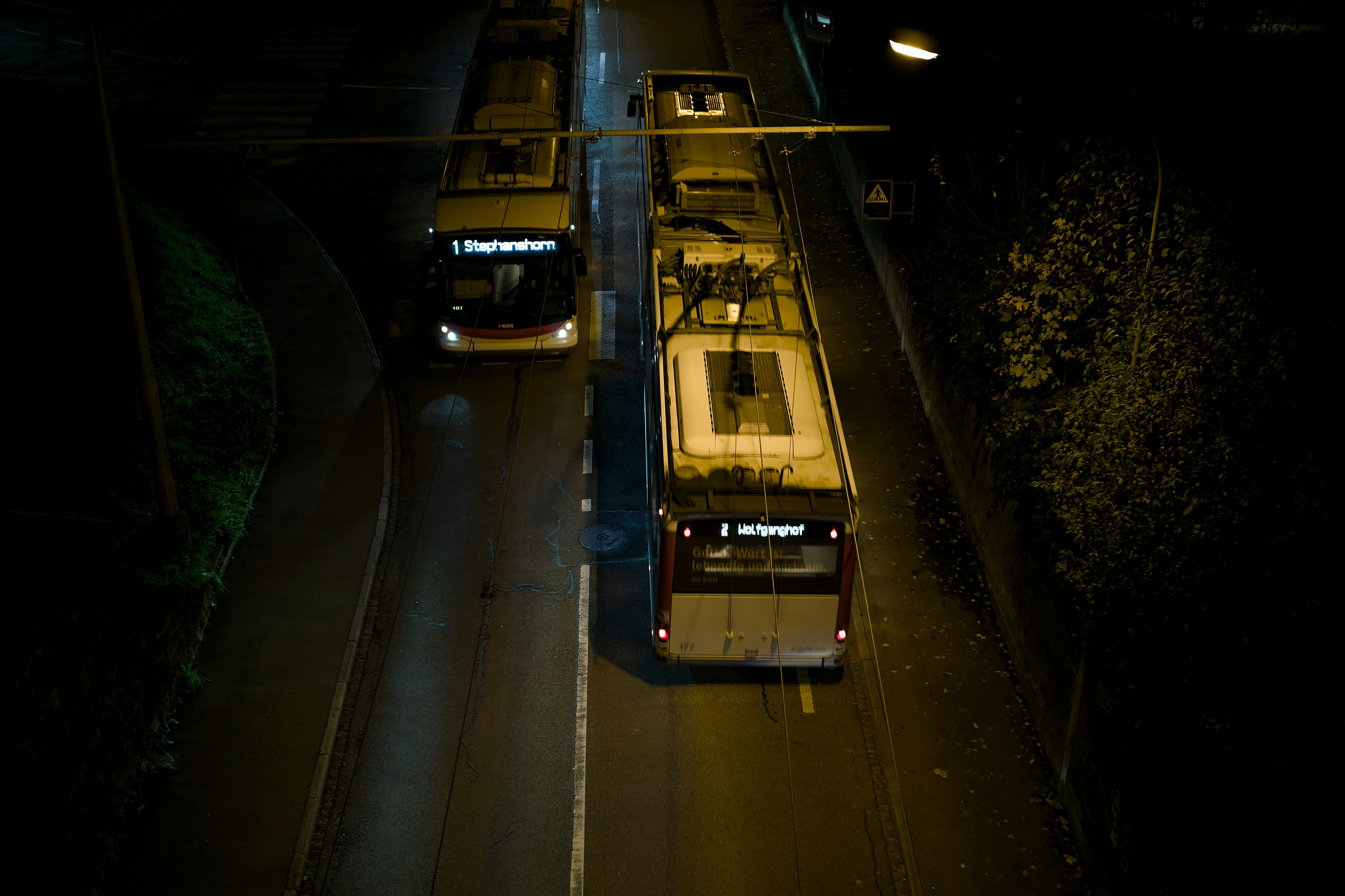 Two buses driving on a road at night.
