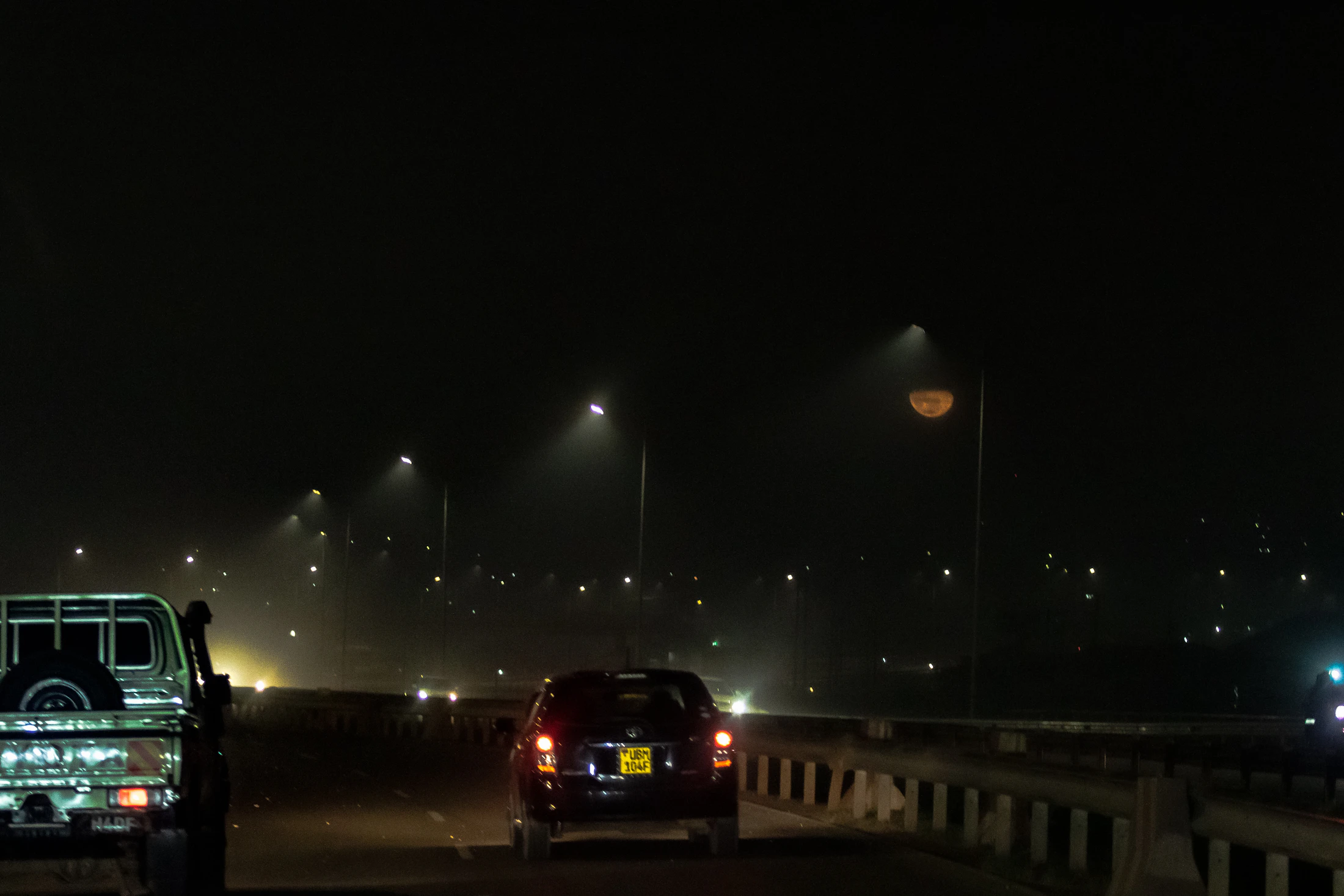 Kampala highway at night with streetlamps, traffic and a foggy Ugandan skyline
