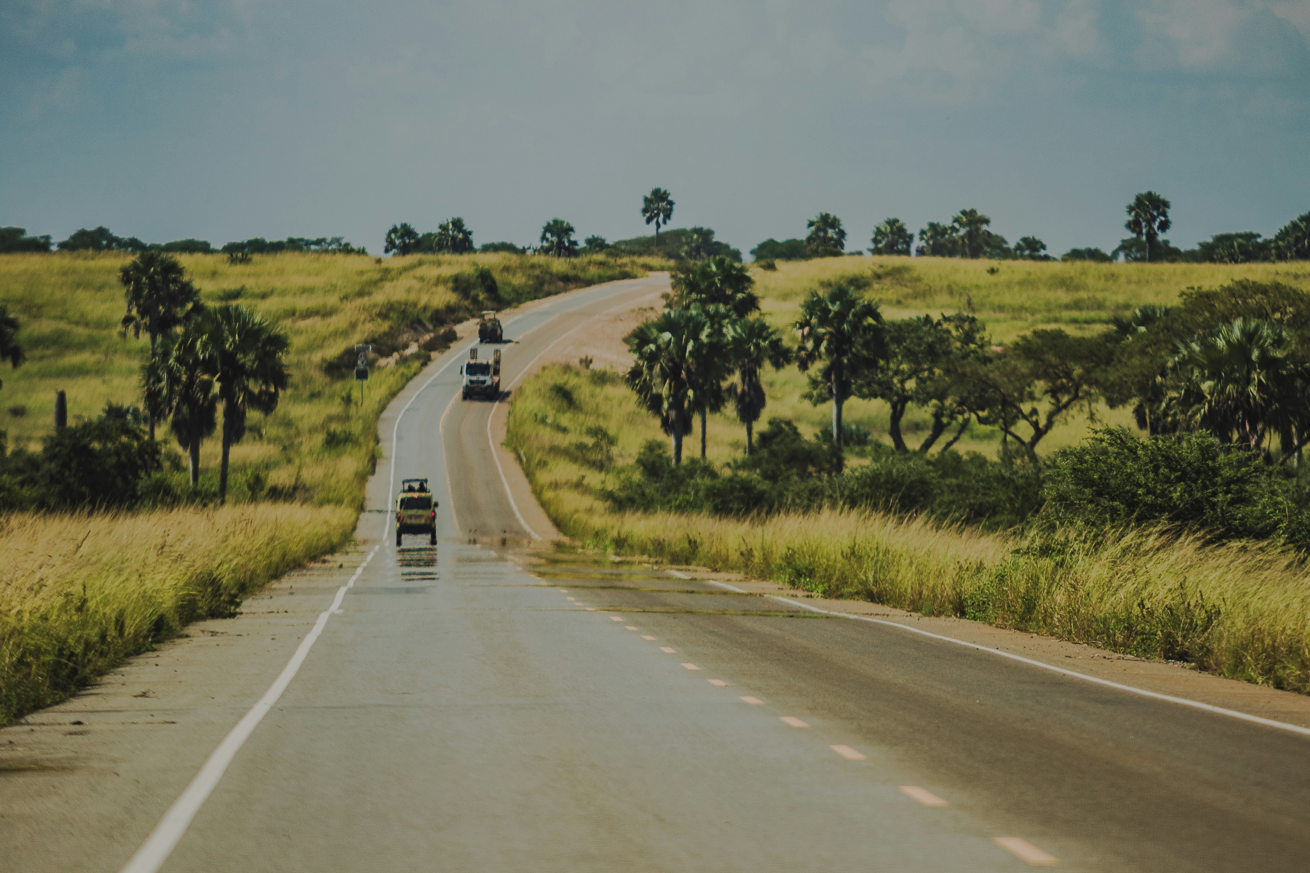 Cars driving on a winding road through grassy hills.