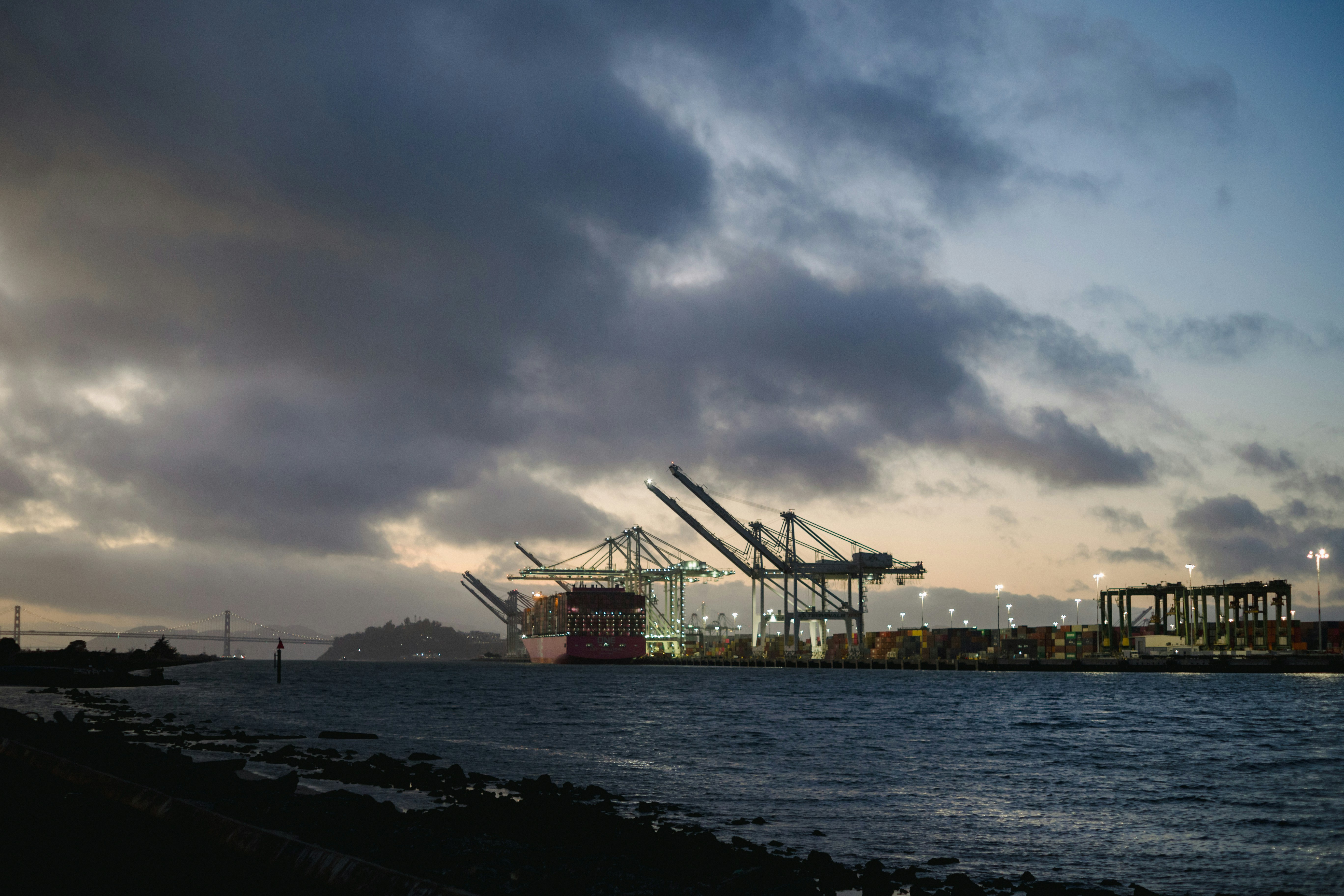 Industrial cranes at a port by the water at dusk.