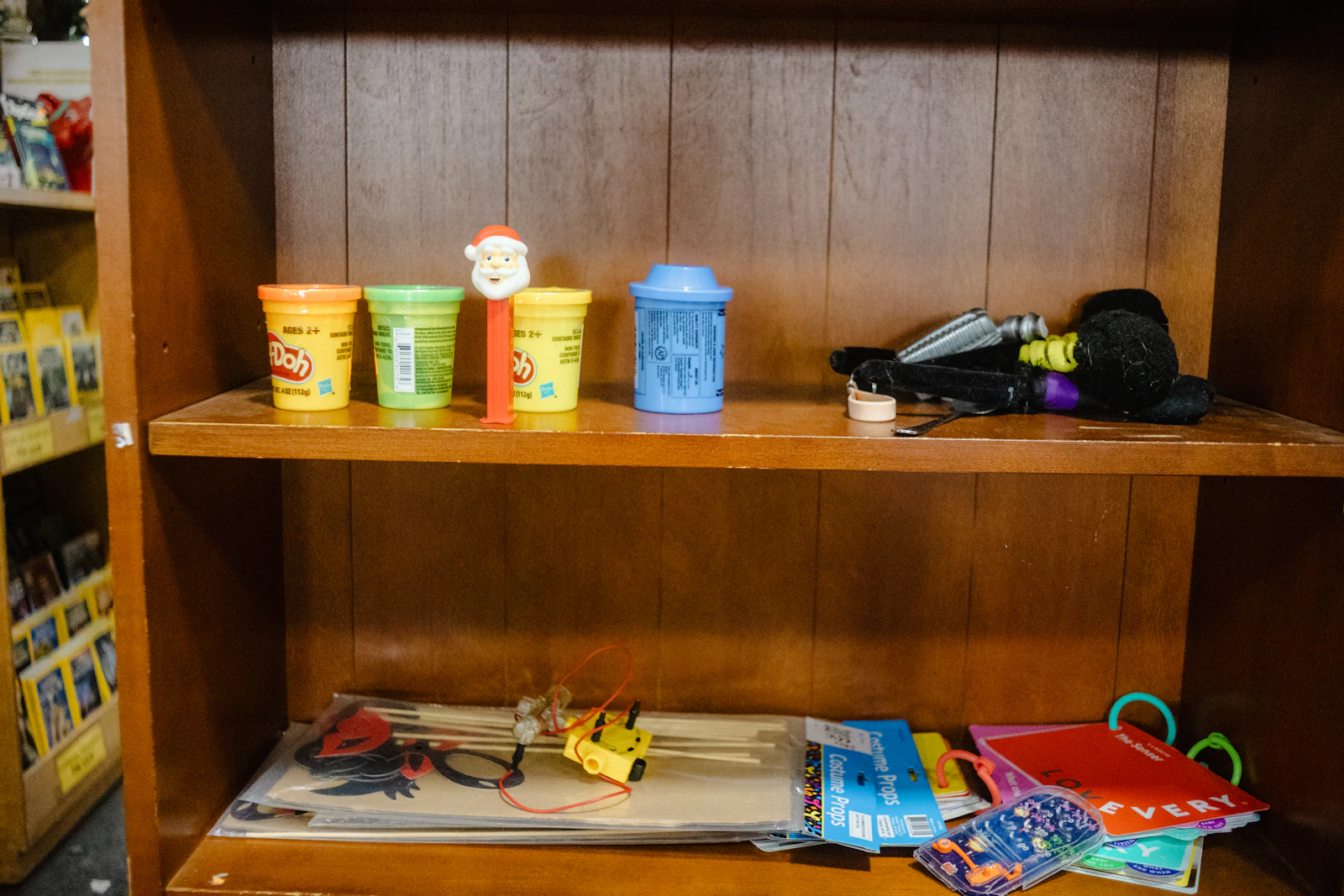 A wooden classroom shelf holding a few tubs of modeling clay, picture books and craft materials