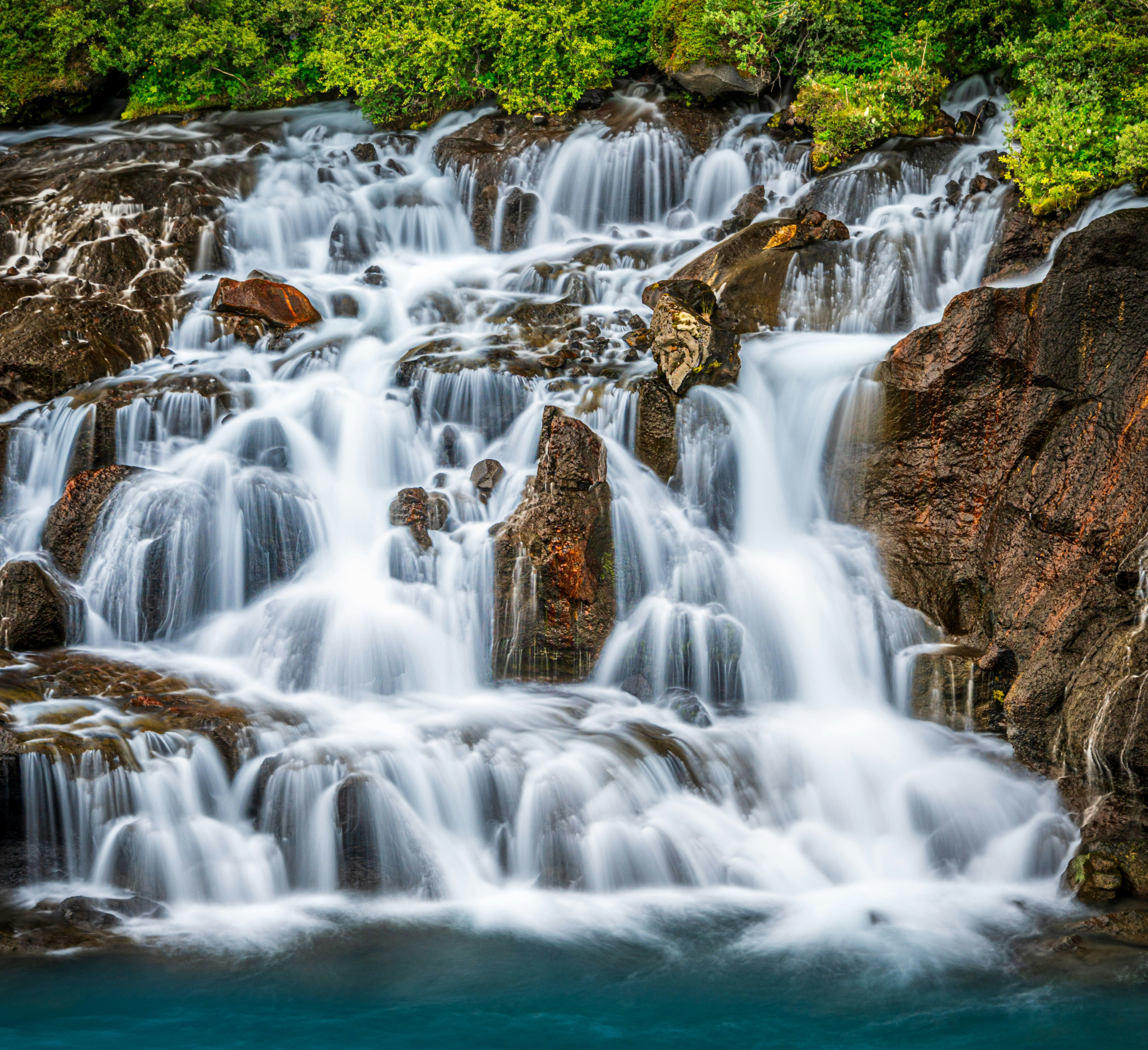 Cascading waterfall flowing over rocks into blue water