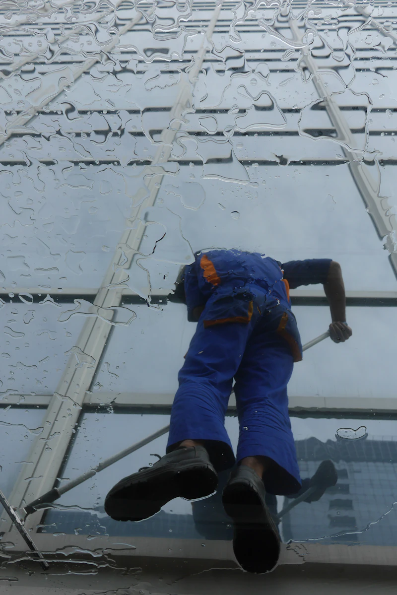 Glasreiniger in blauer Arbeitskleidung mit Abzieher auf einem Glasdach