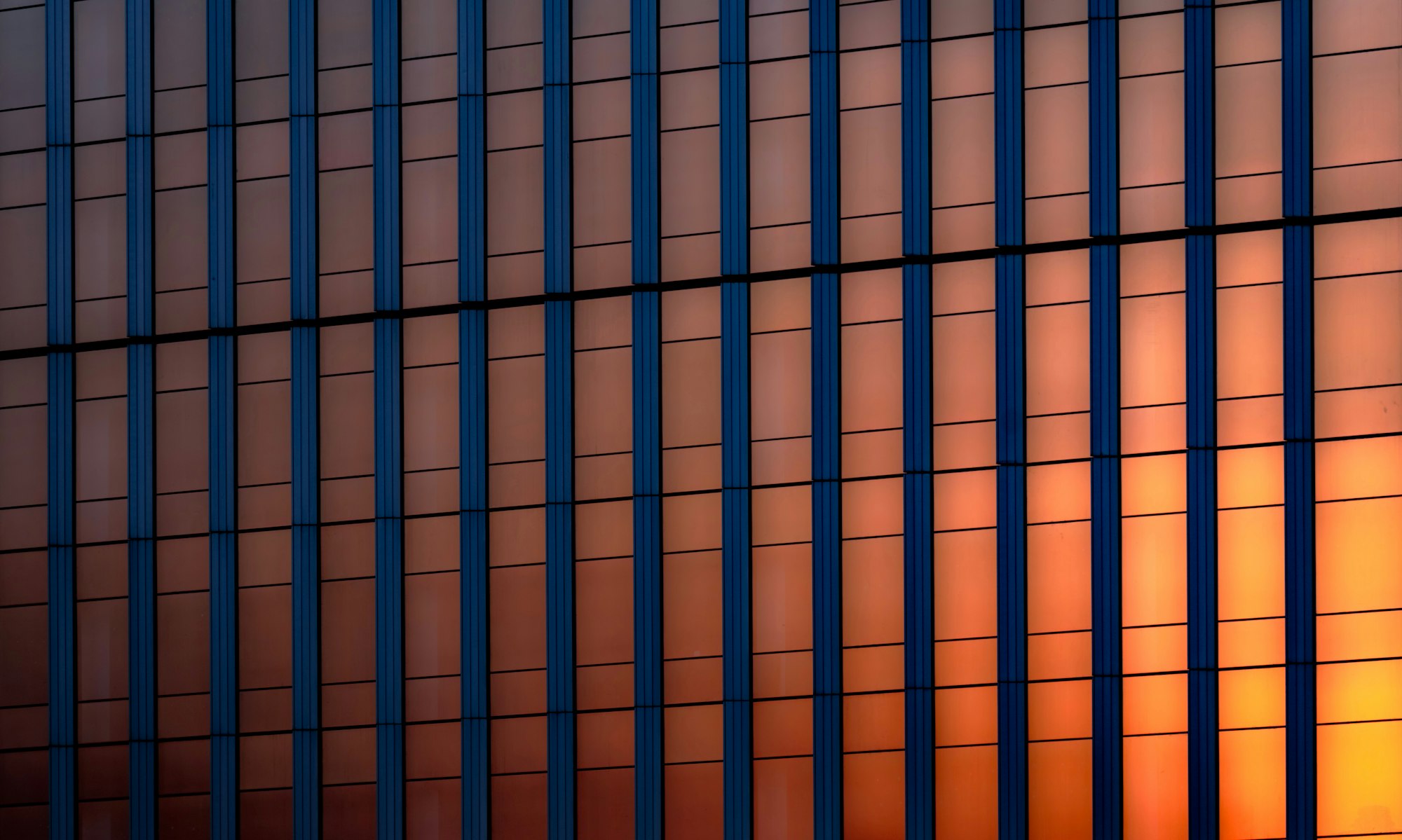 Blue-mullioned glass curtain wall glowing orange with sunset light shining through