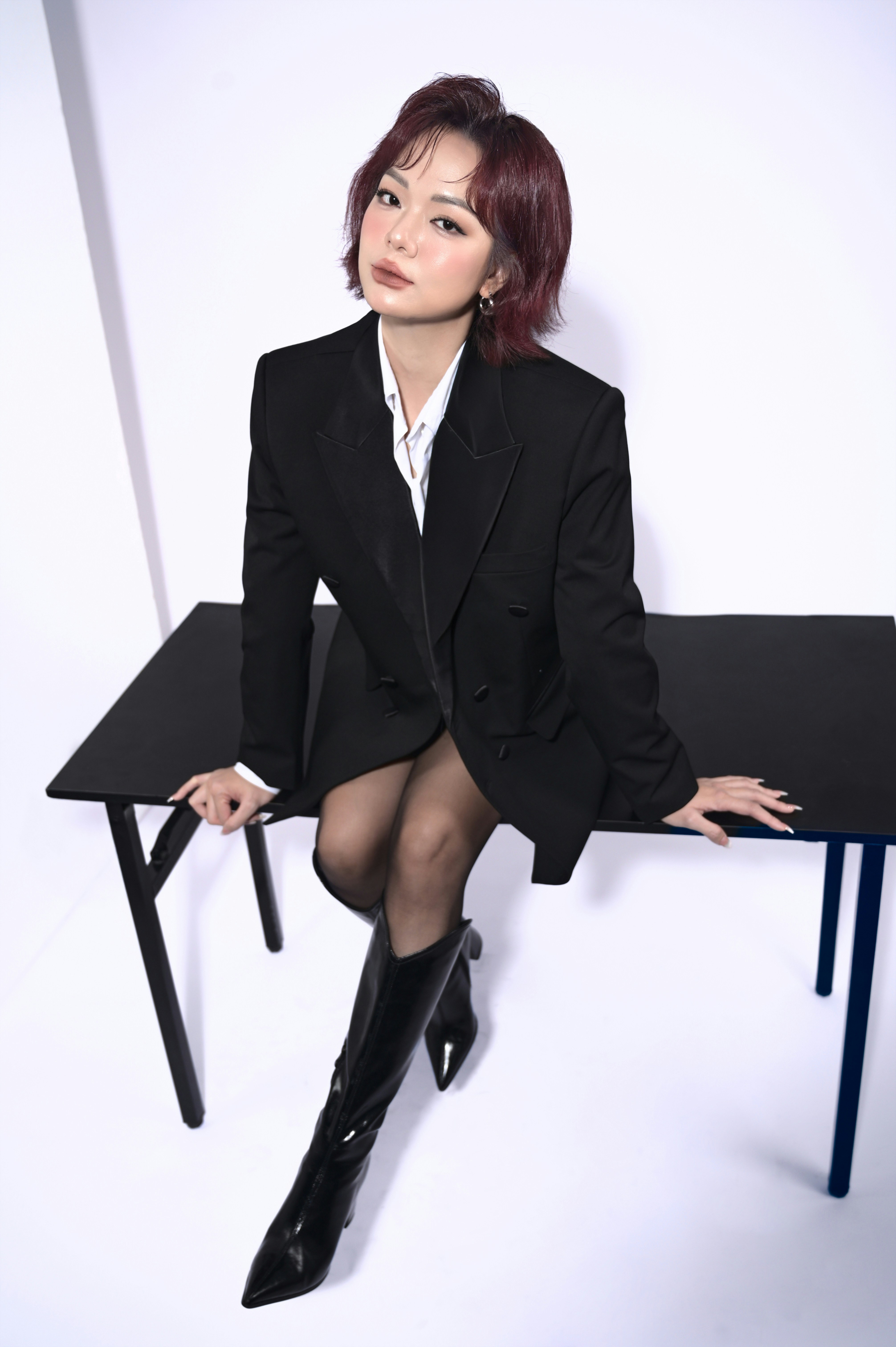 Young woman in black blazer sits on table.