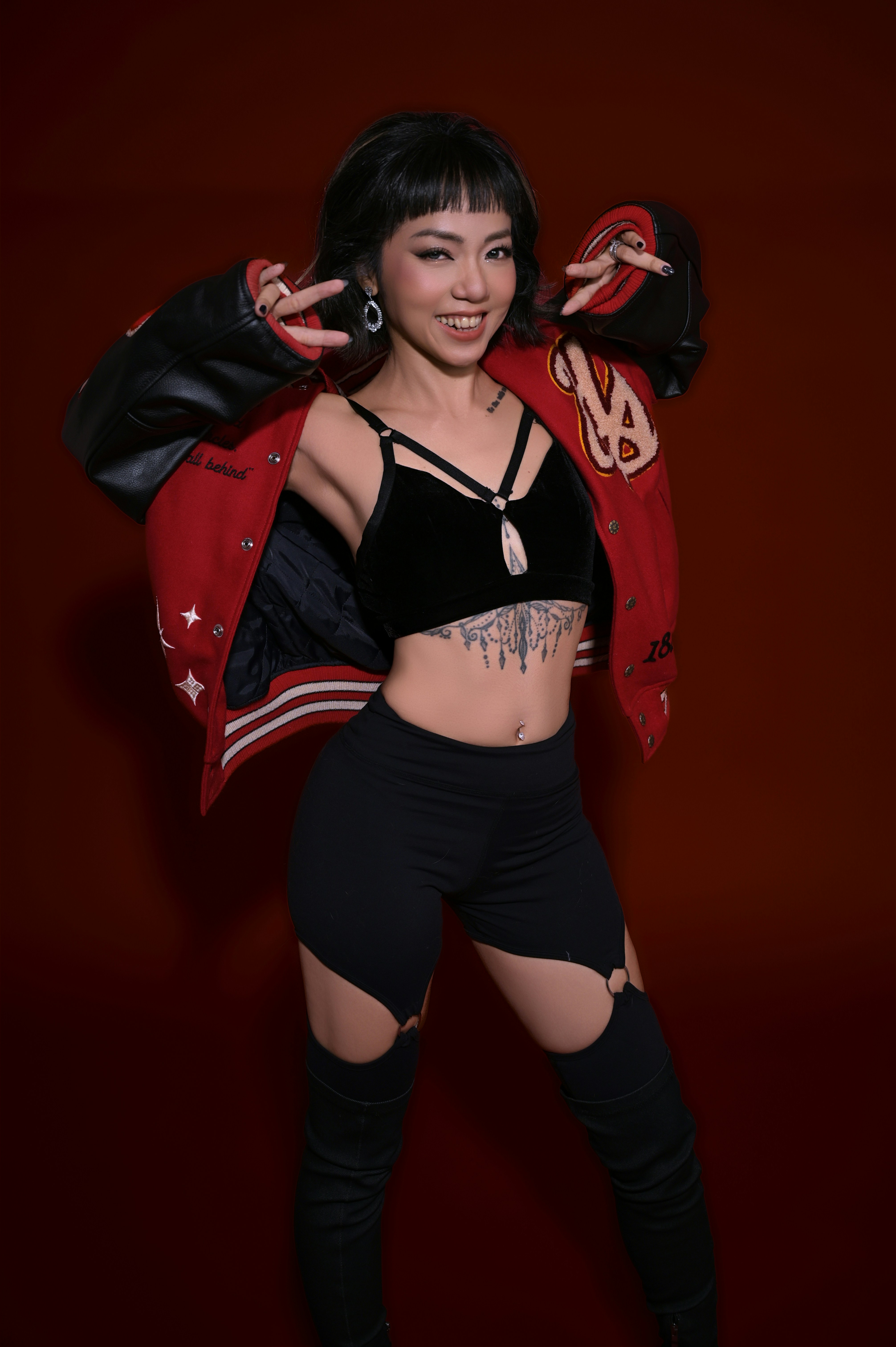 Woman in varsity jacket and black outfit posing