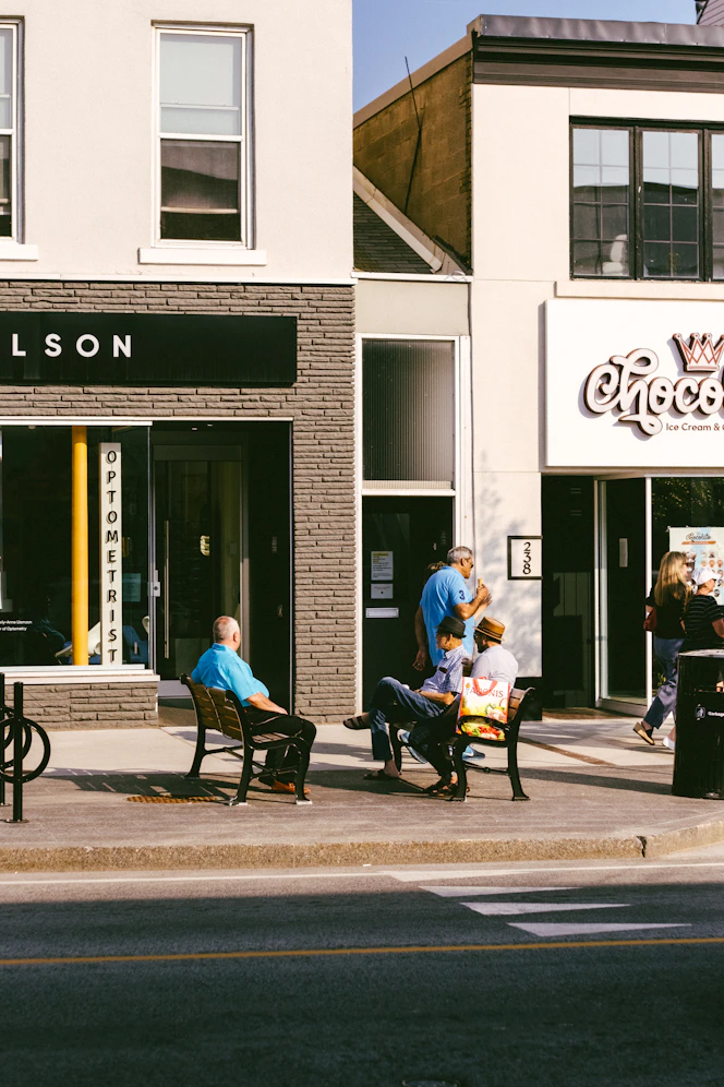 People sitting on benches outside shops on a sunny day.