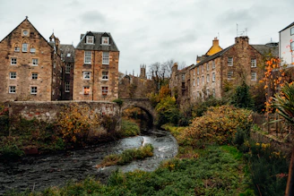 Stone buildings line a river with autumn foliage.
