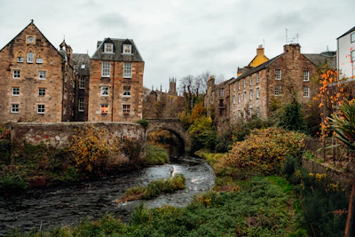 Stone buildings line a river with autumn foliage.