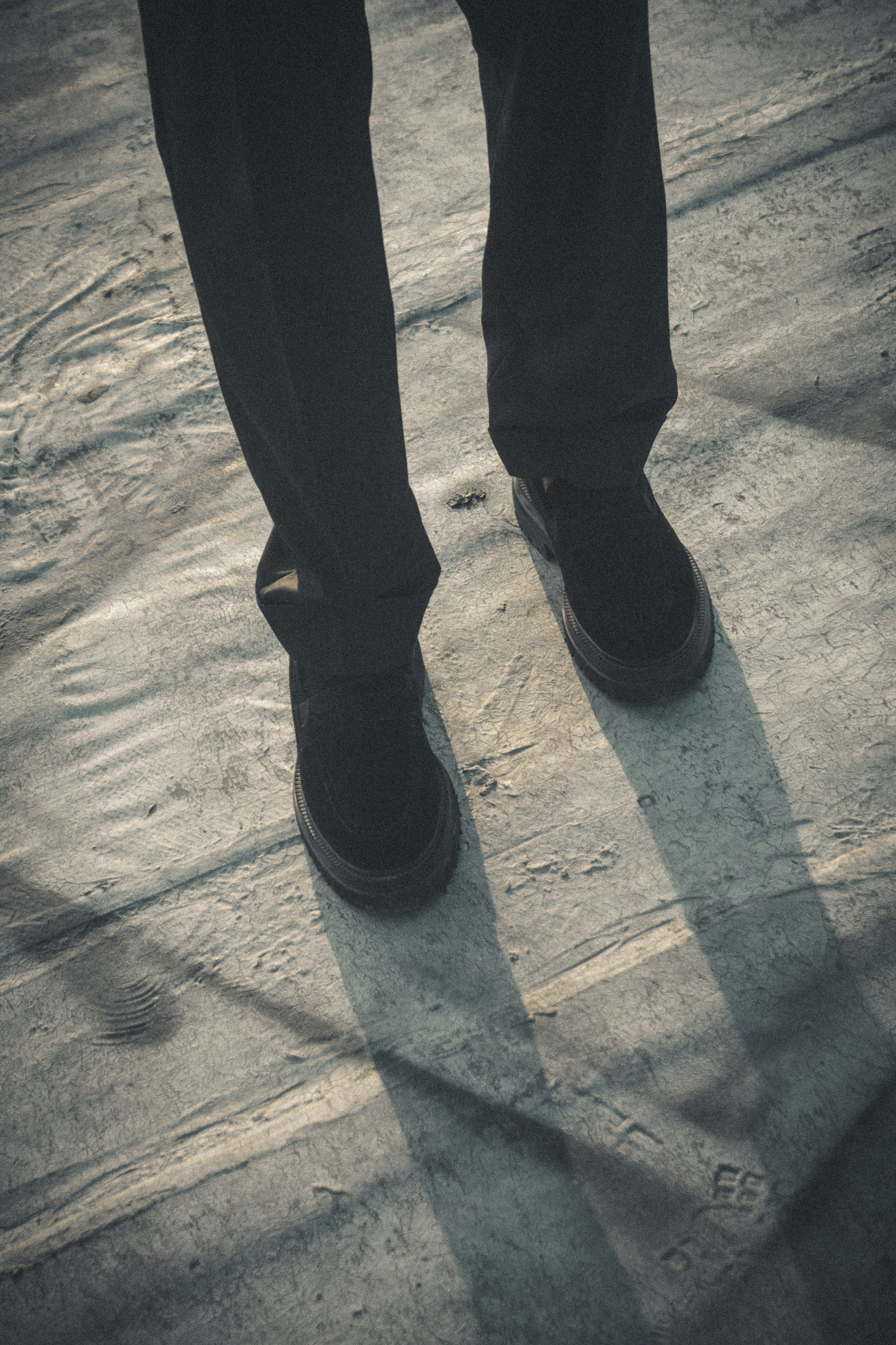 Person standing on textured ground with shadows.