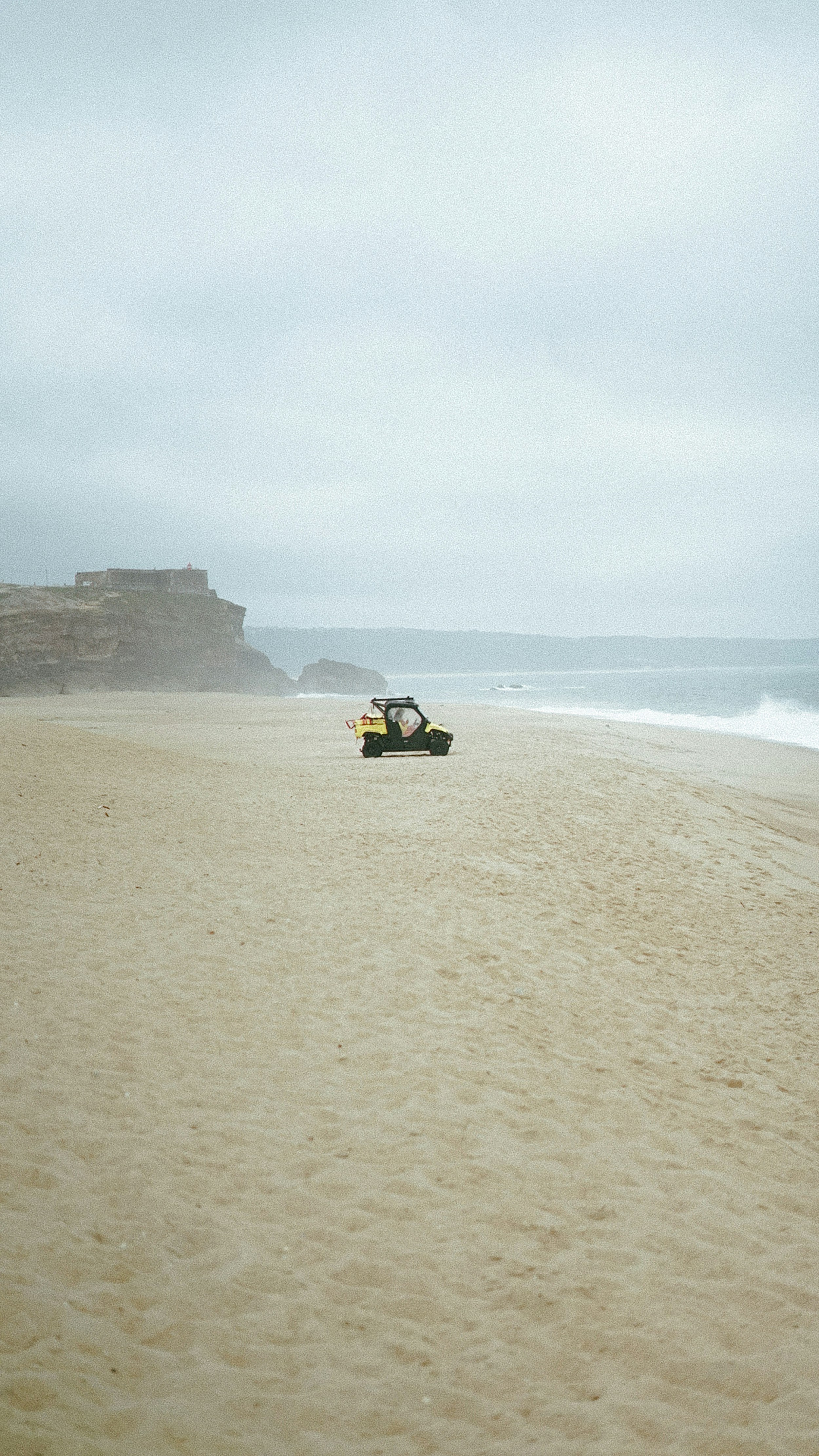 崖の近くの砂浜にバギーが停まっています。
