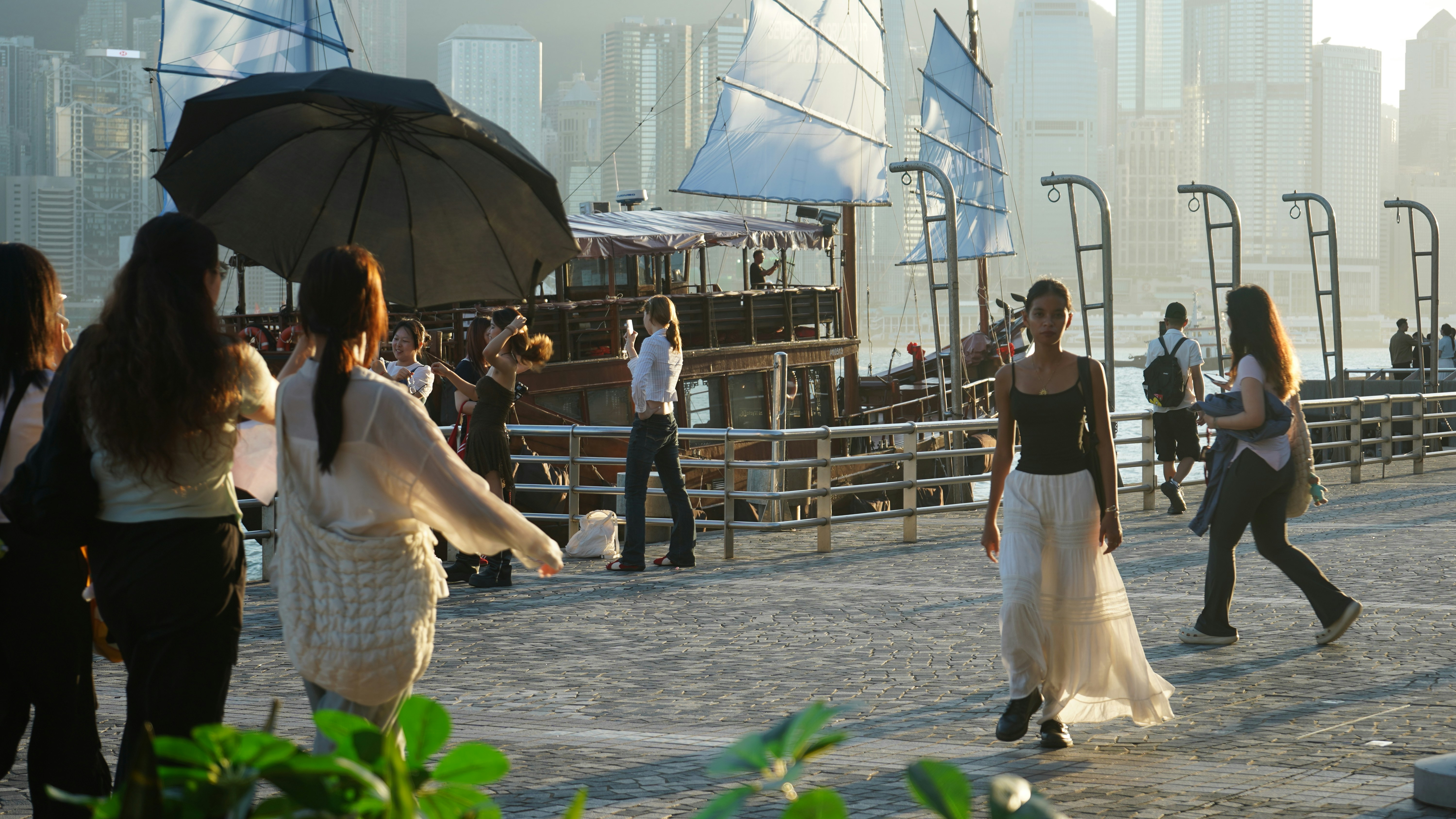People walk along a waterfront with traditional boats.
