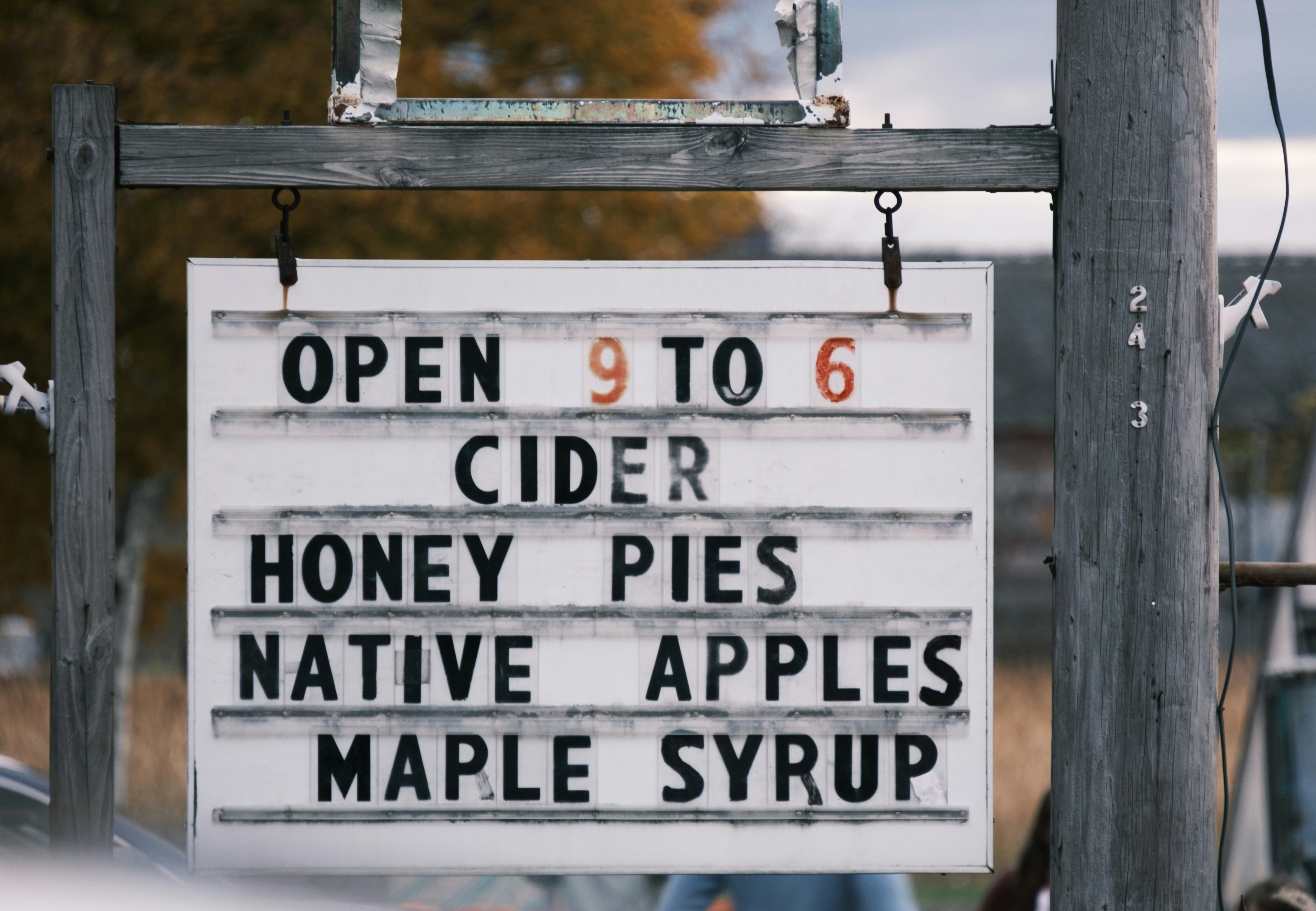 Farm stand sign lists cider, honey, pies, apples, syrup