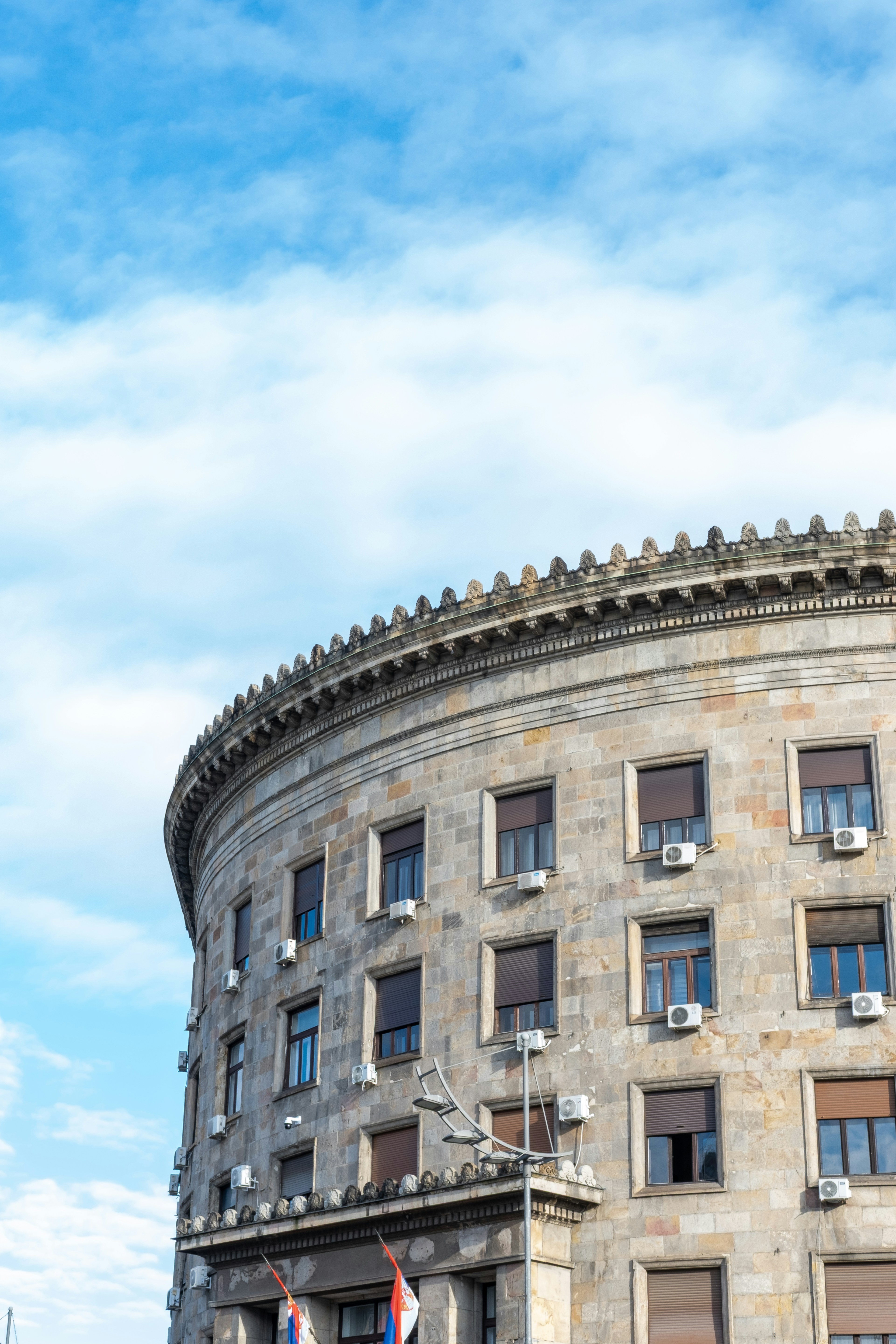 Curved stone building with many windows under blue sky