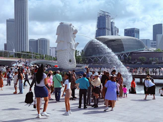 Crowds gather around the merlion statue with city skyline.