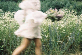Woman in white dress holding flowers in a field.