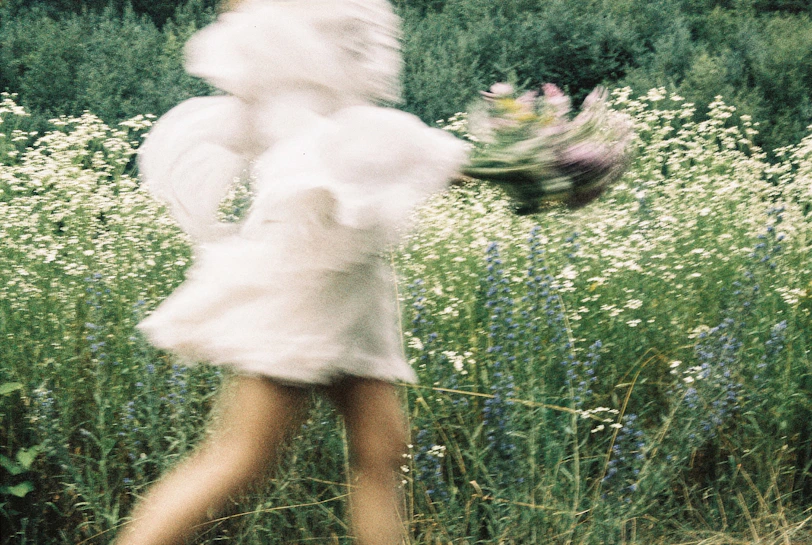 Woman in white dress holding flowers in a field.
