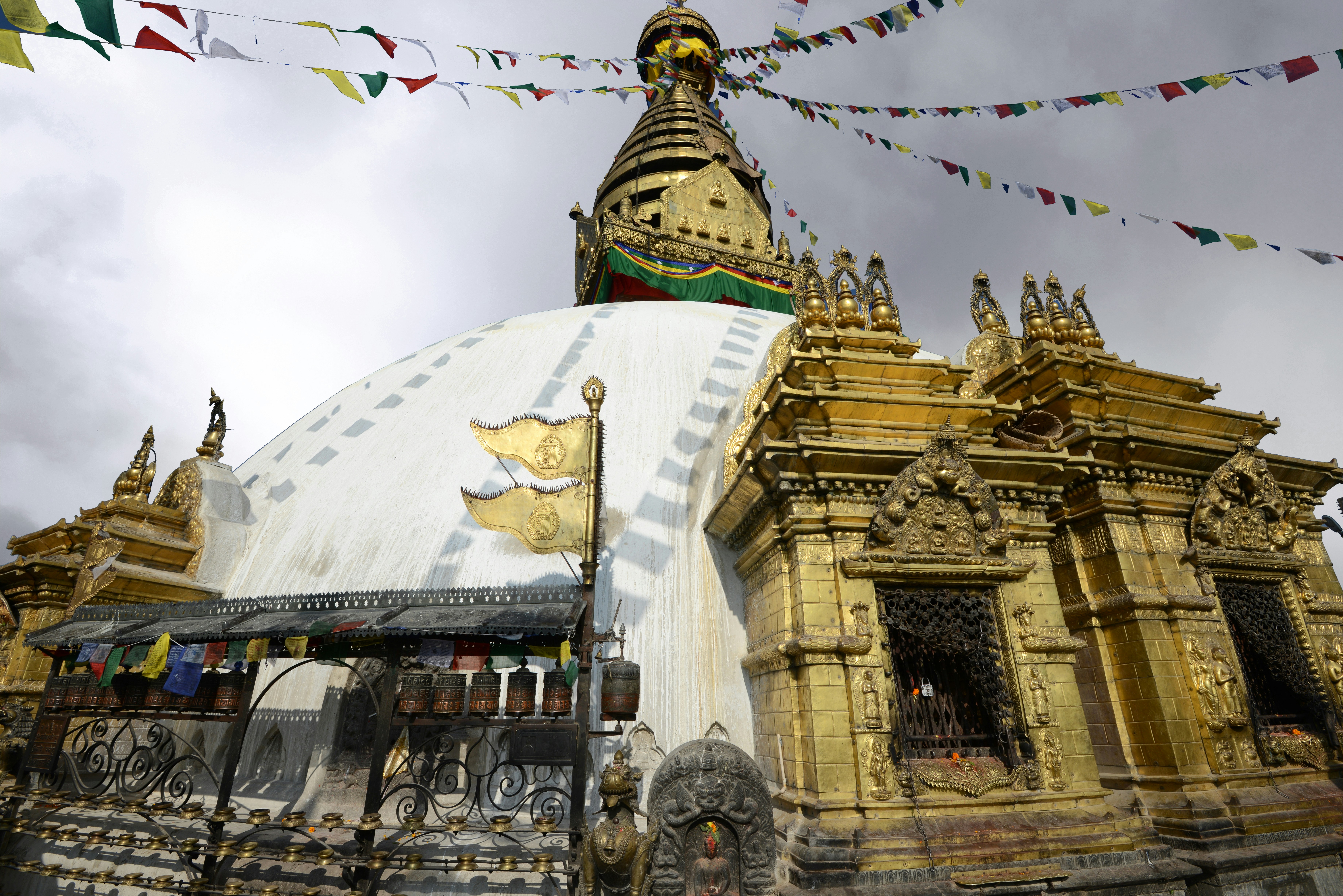 Golden stupa with prayer flags under cloudy sky.