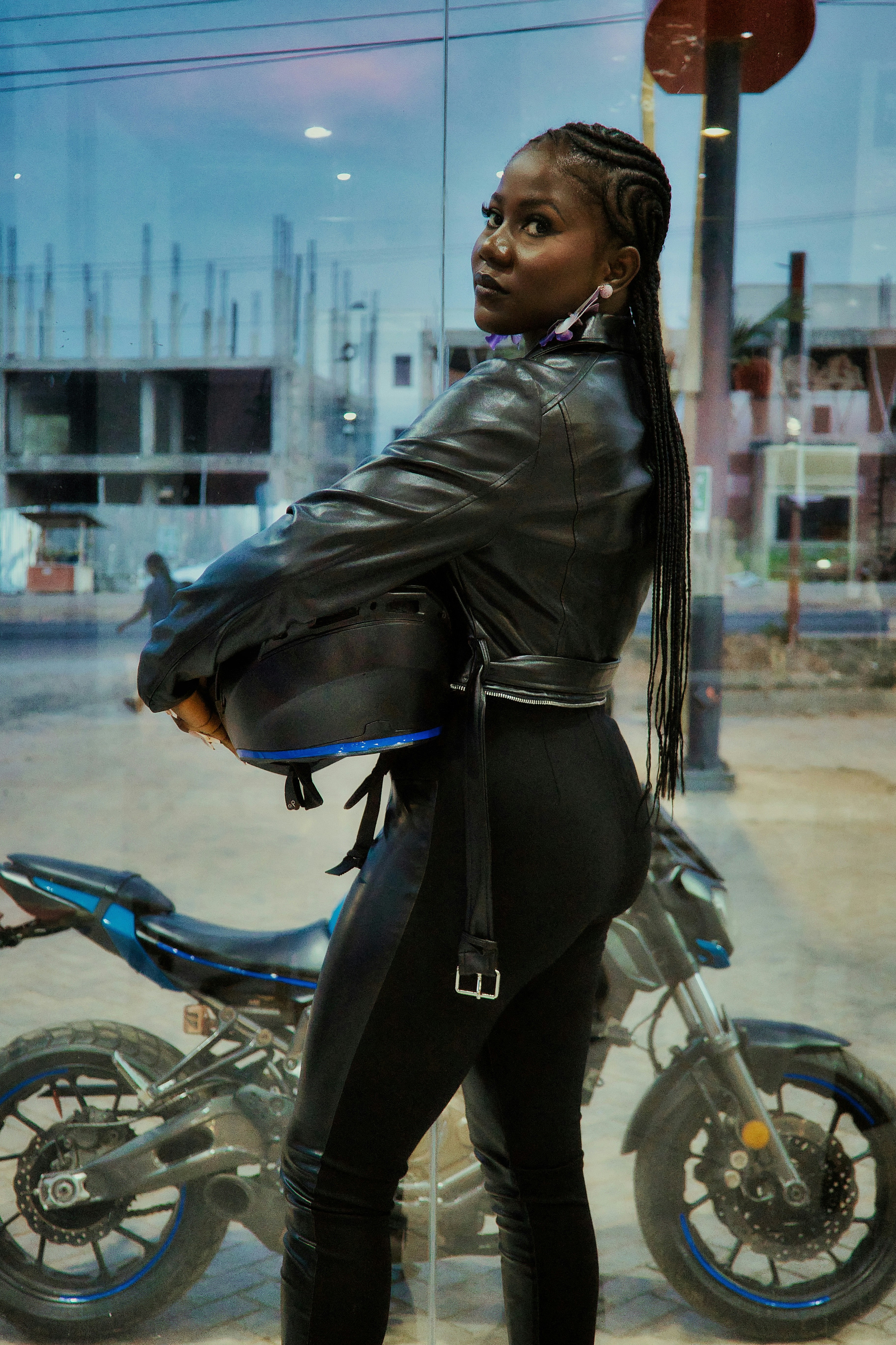 Woman in leather jacket holding helmet near motorcycle