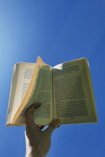 Hand holding open book against blue sky