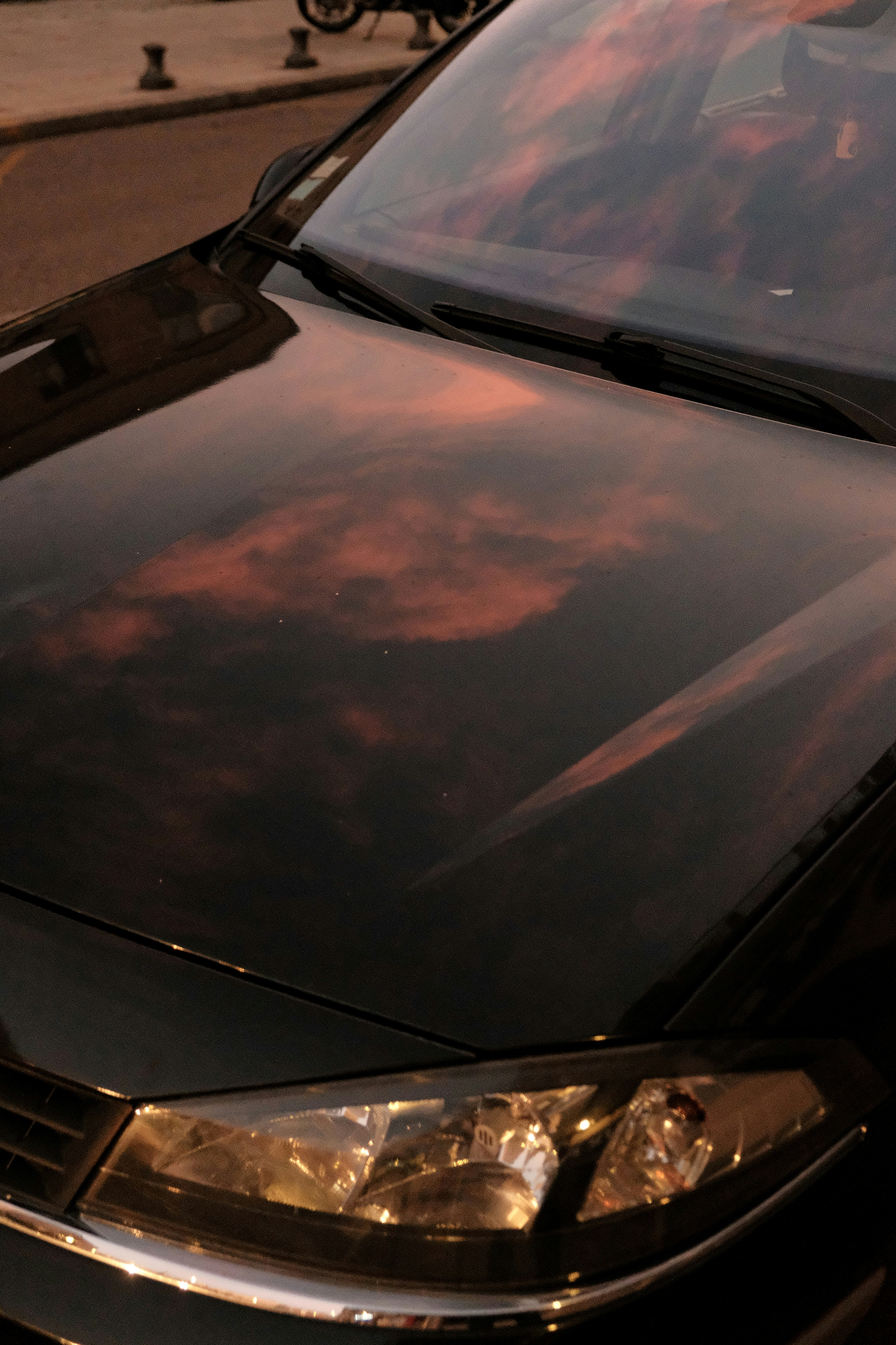 Sunset clouds reflected on a car hood.