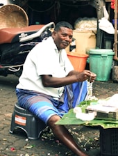 Man making a flower garland at a market stall.