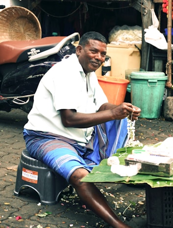 Man making a flower garland at a market stall.
